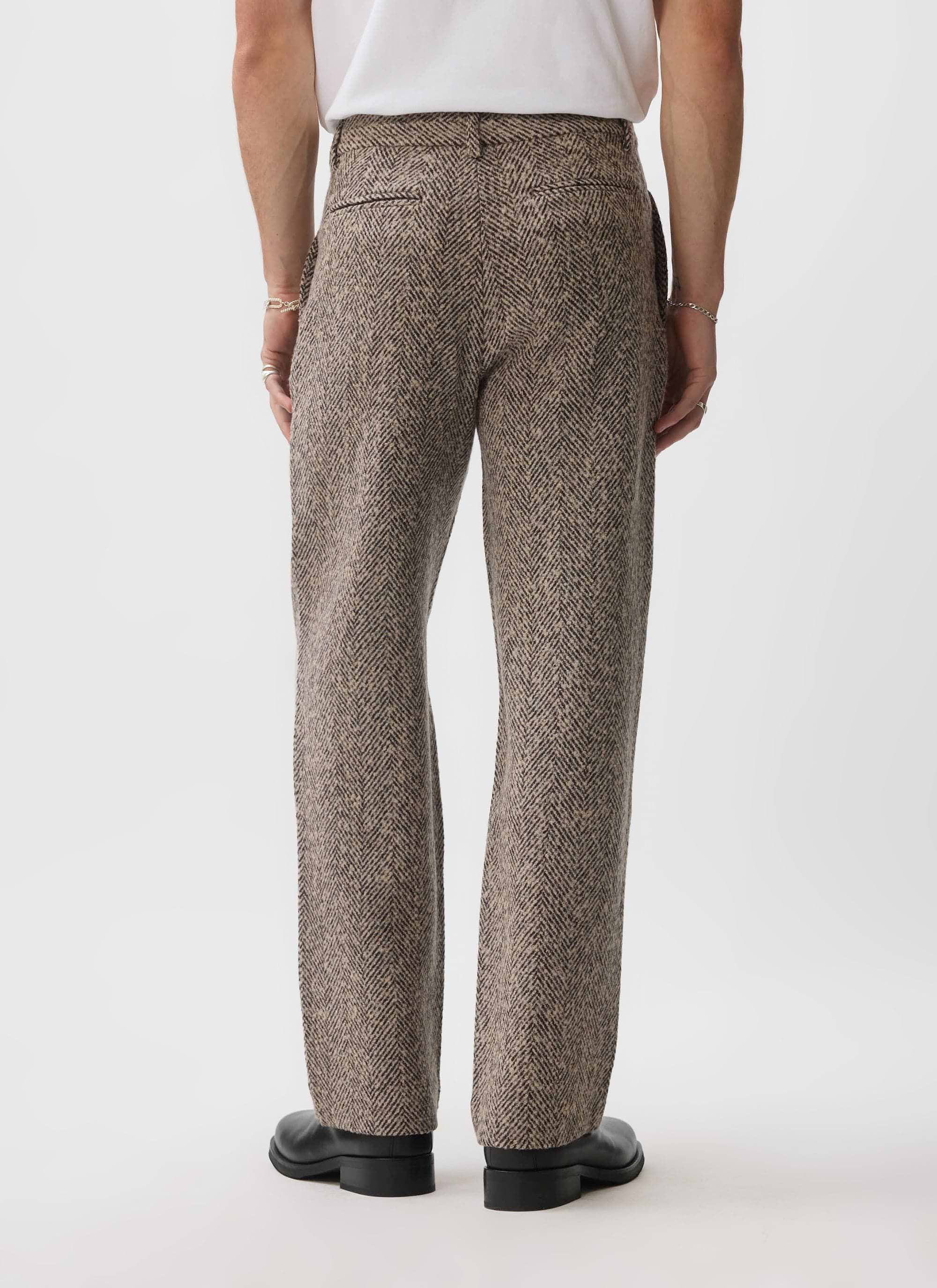 A model from behind showing the straight leg fit of the Percival Herringbone Trousers in an ecru wool blend.