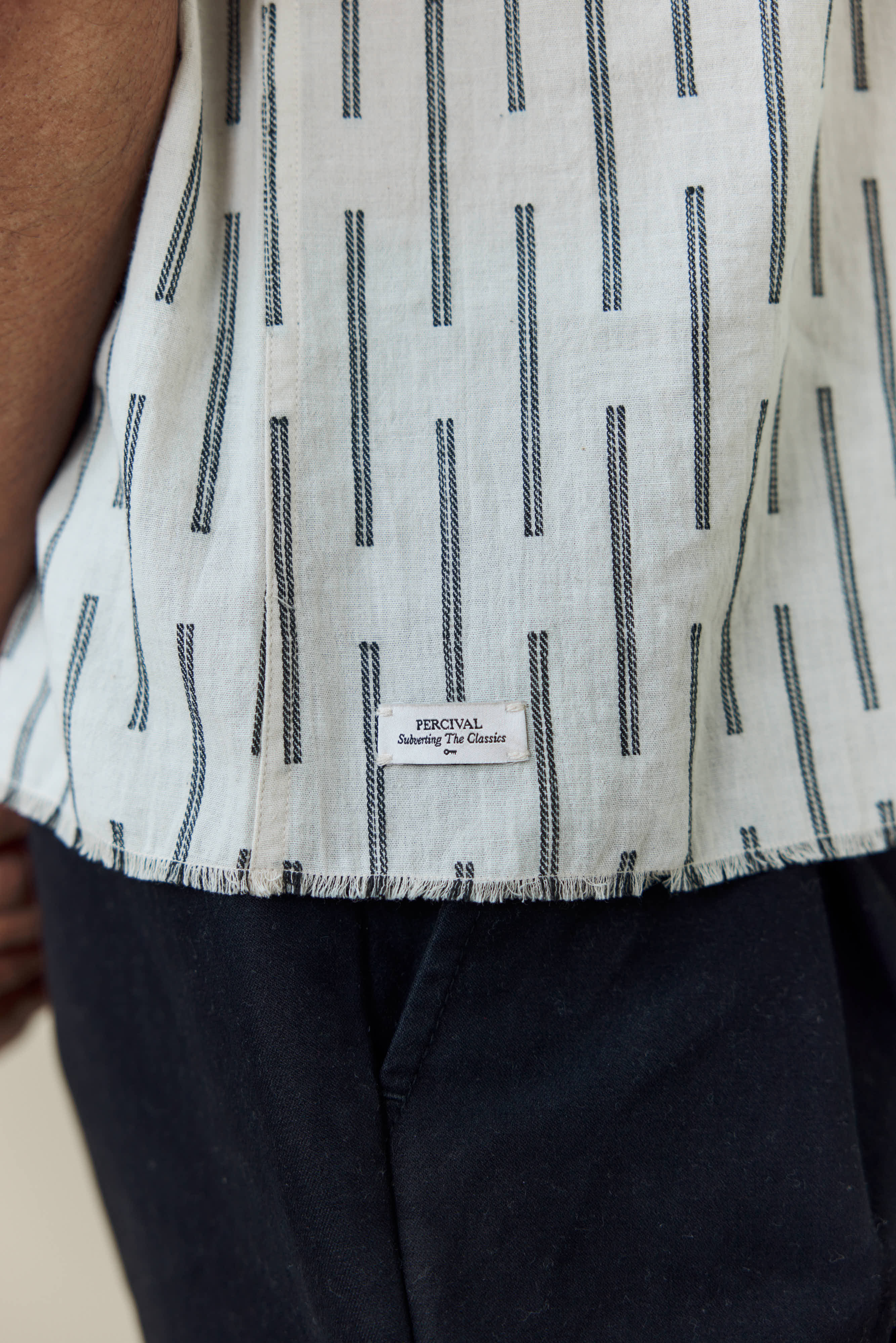 Close-up of the Percival Nancy Boxy Shirt in ecru, showing the jacquard stripe detail, frayed hem and branded label.