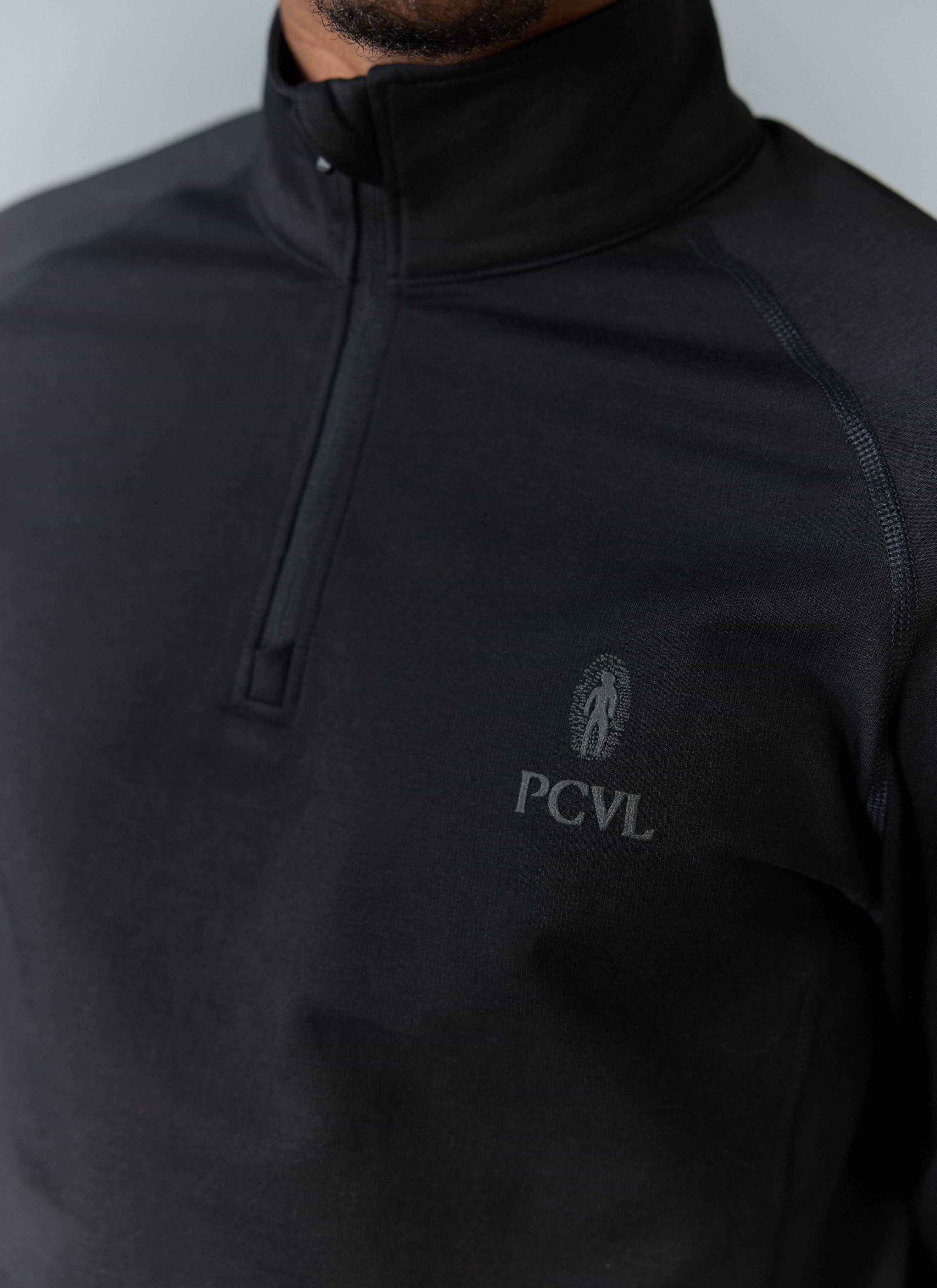Close-up of a model wearing the black PCVL Base Layer Quarter Zip by Percival, showing the subtle reflective chest logo.