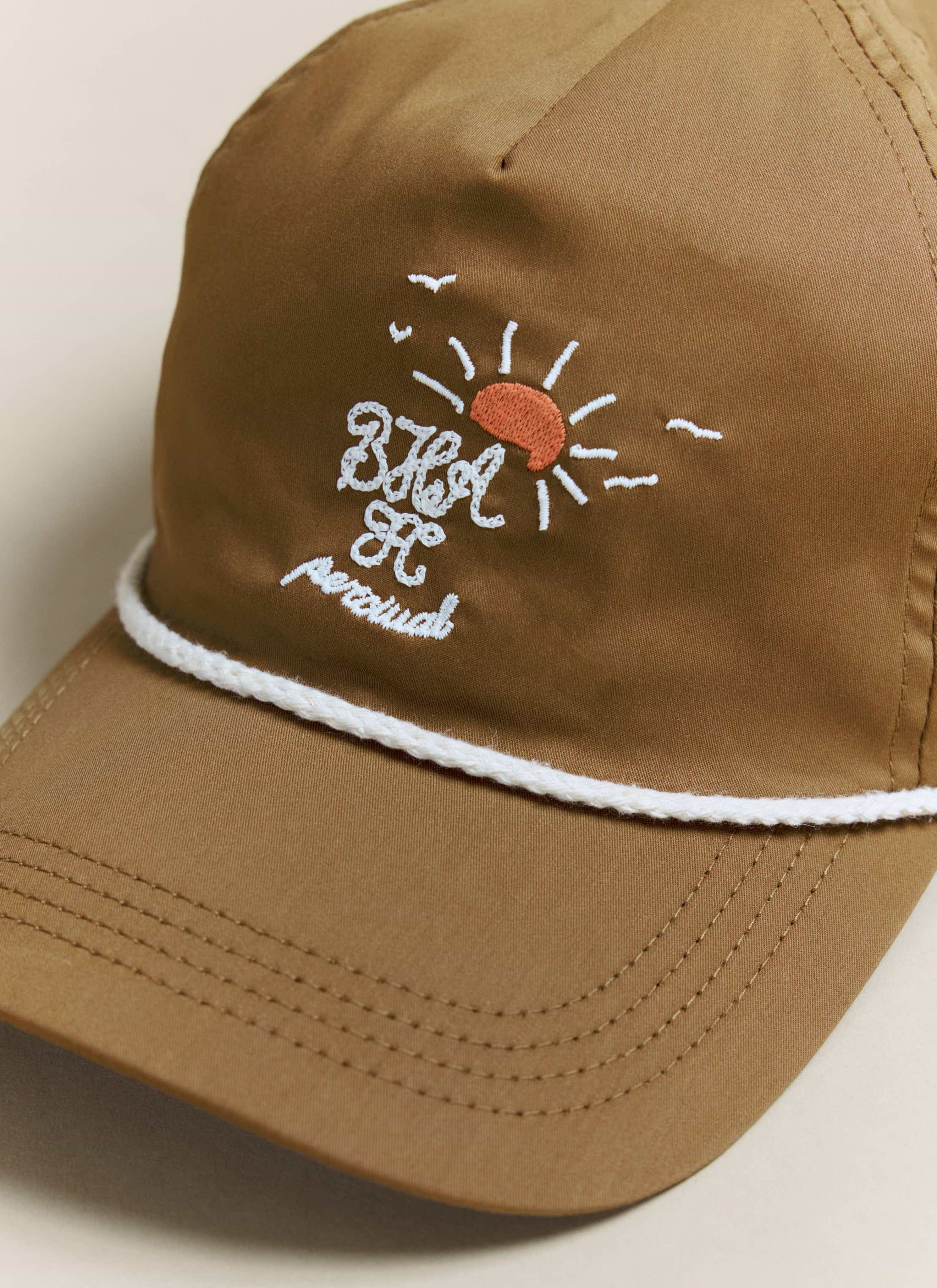 Close-up of the embroidered logo on the Percival x Brighton & Hove Albion F.C. rust trucker cap, with white rope detail.