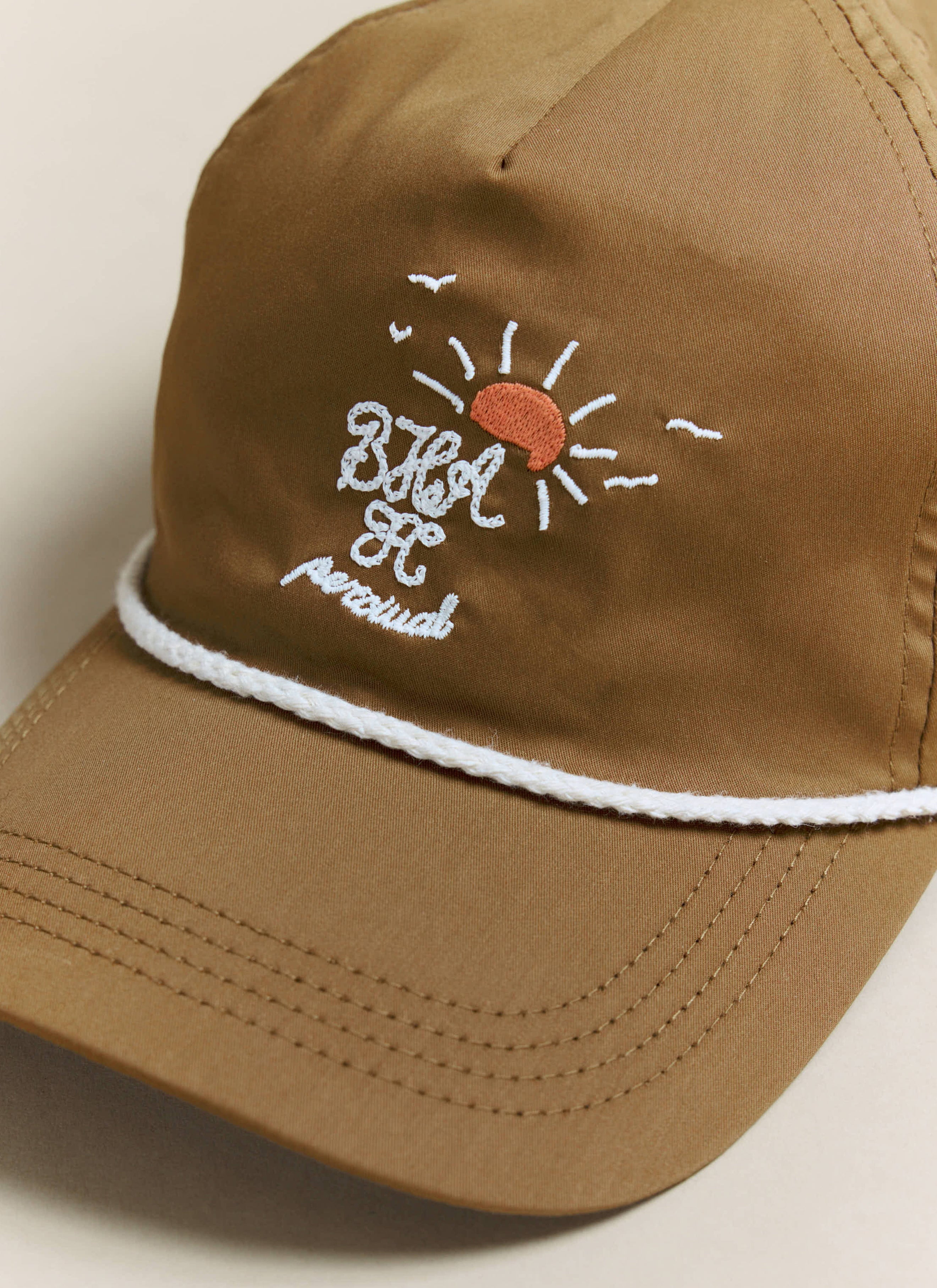 Close-up of the embroidered logo on the Percival x Brighton & Hove Albion F.C. rust trucker cap, with white rope detail.