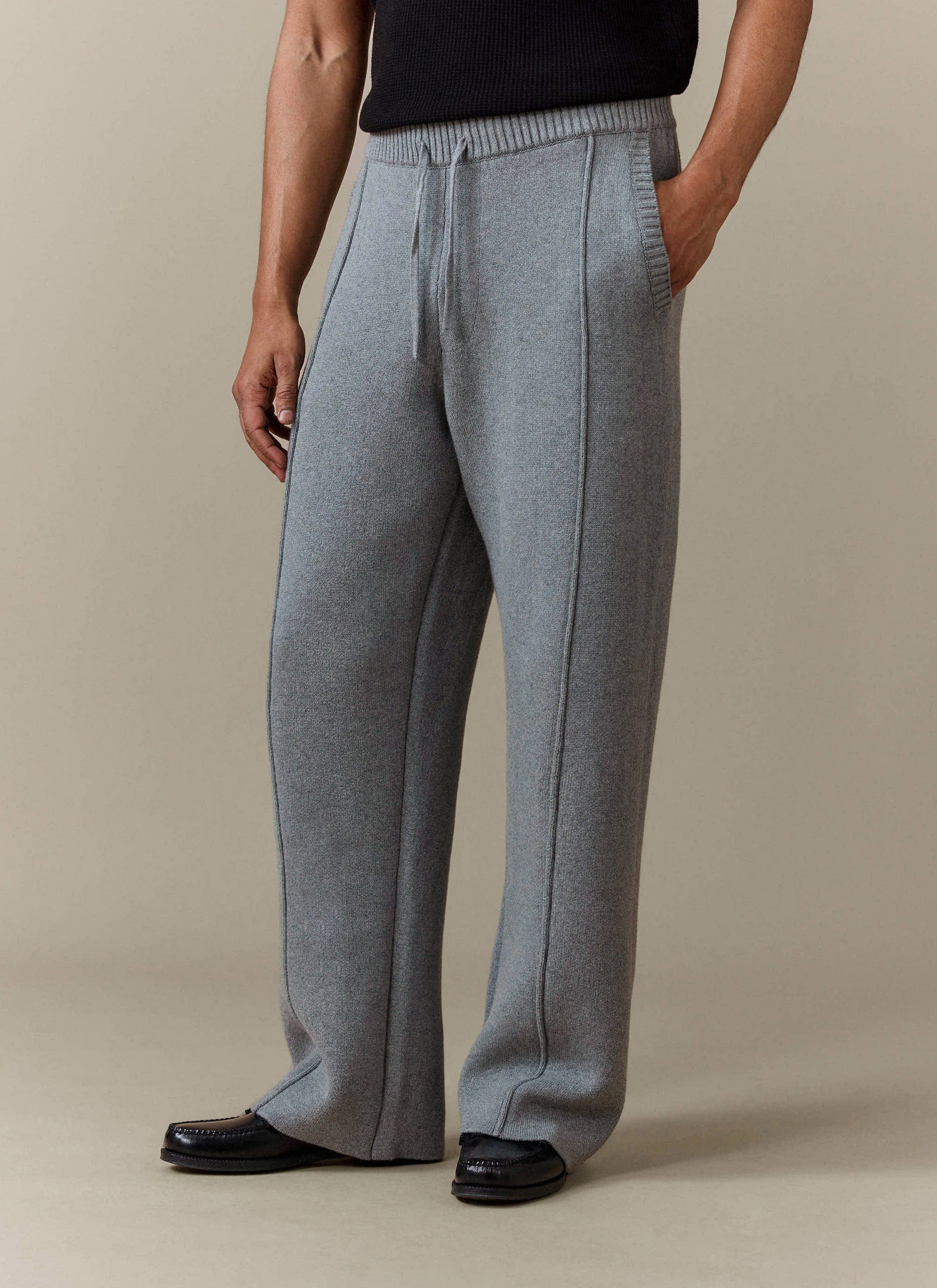 A model wears the Percival Chronicle Knitted Straight Leg Trackpant in grey, styled with a black top and smart loafers.