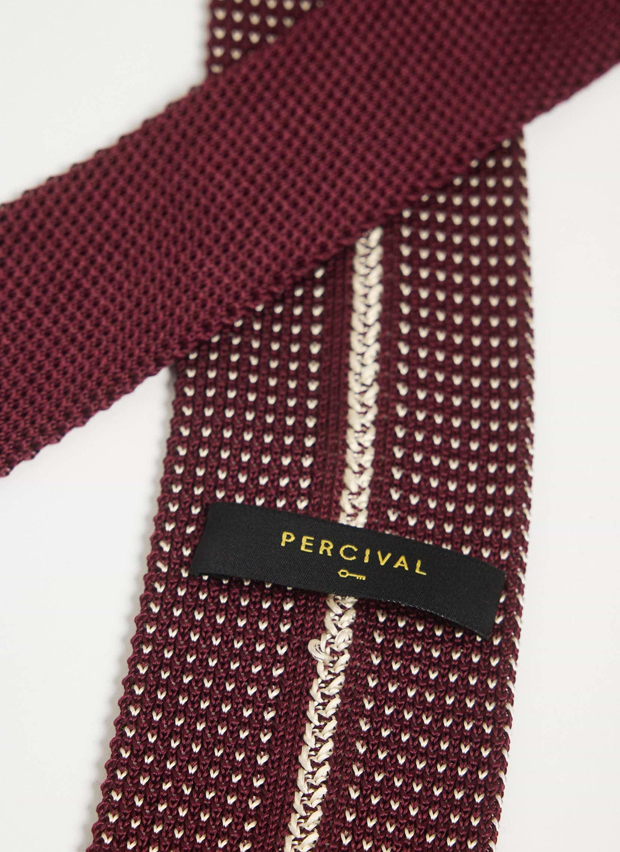 A close-up of the Percival red Birdseye Silk Tie, showing the intricate knit texture and the brand label.