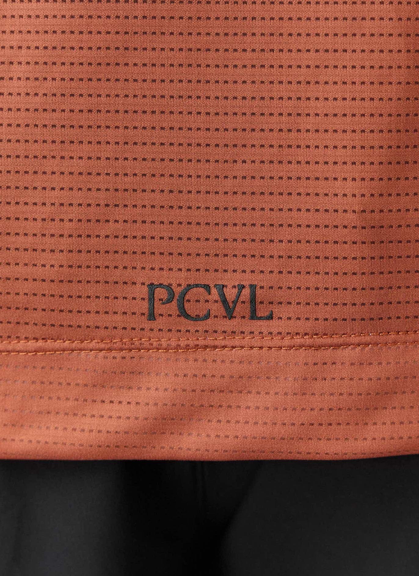 A close-up of the Percival PCVL Printed Performance Top in rust, showing the black printed logo and breathable fabric.