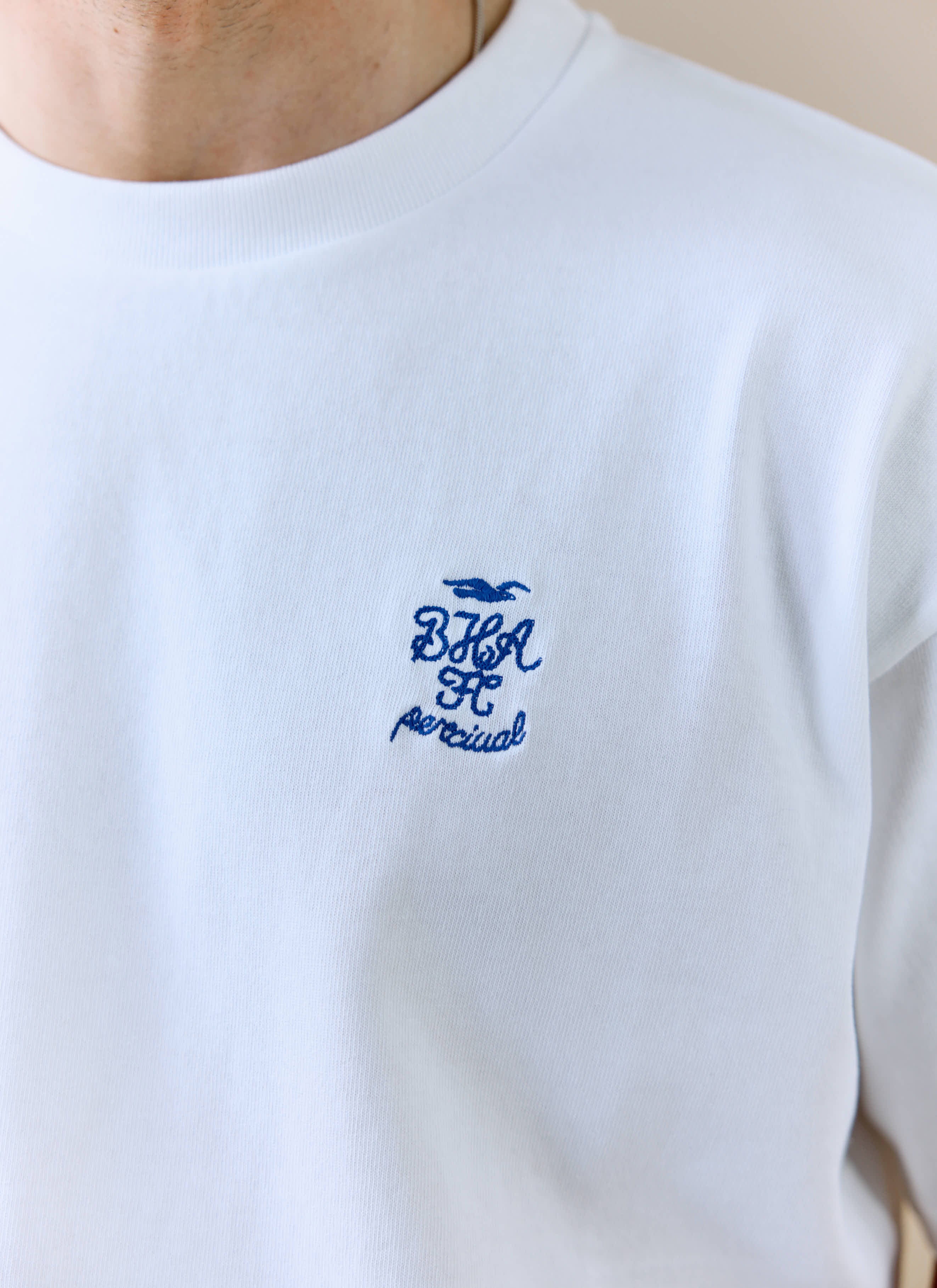 A close-up of the blue embroidered Brighton & Hove Albion F.C. logo on the white Archive Kits T-shirt by Percival.