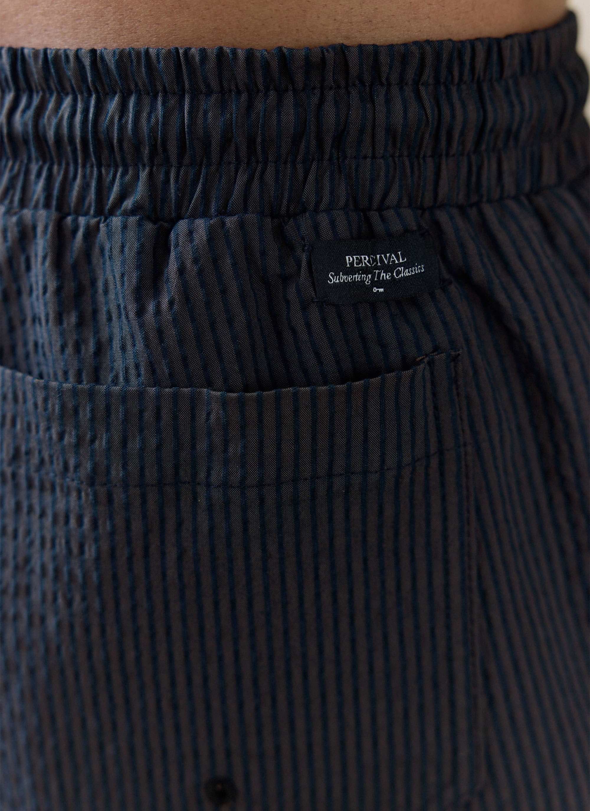 Close-up of the navy stripe seersucker cotton fabric and brand tag on the Rowan Swim Shorts by Percival.