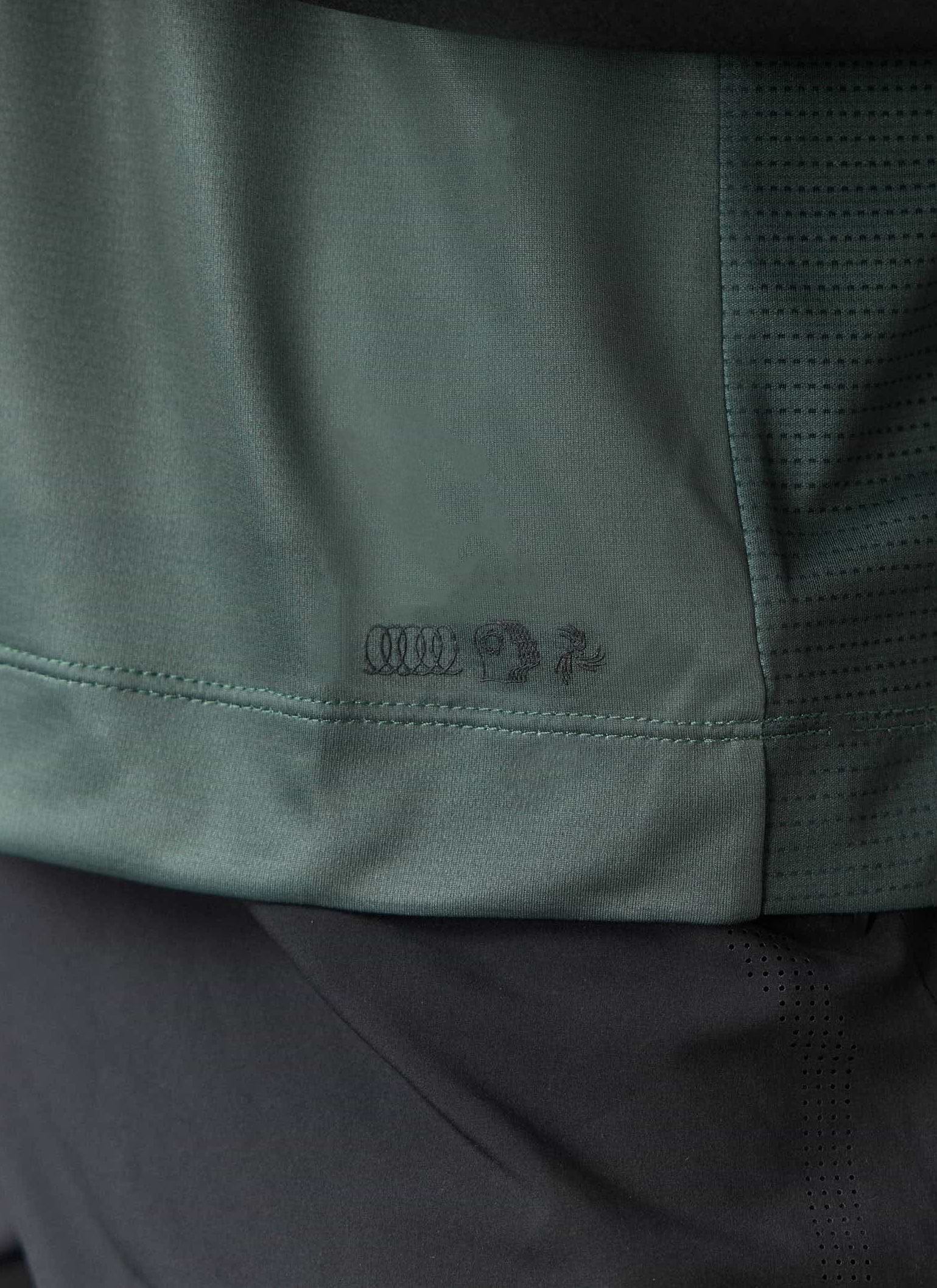 A close-up of the Percival PCVL Printed Performance Top in forest, showing the tonal logo and perforated panel.