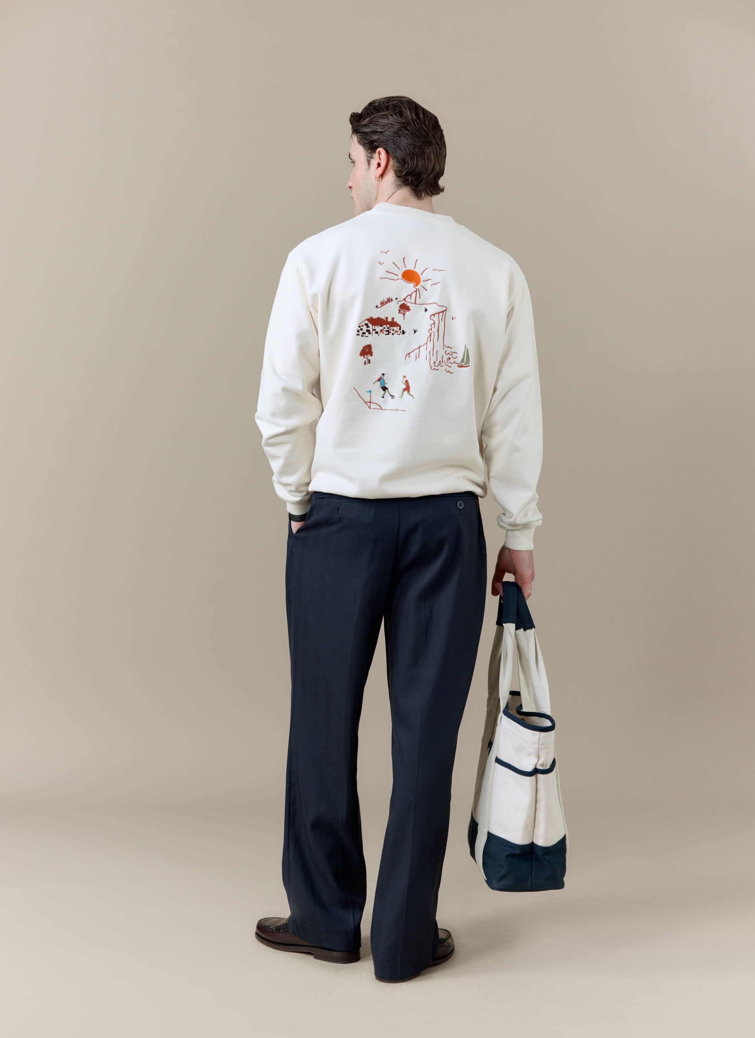 A model seen from behind wearing the Percival x Brighton F.C. cream sweatshirt, carrying the navy and cream tote bag.
