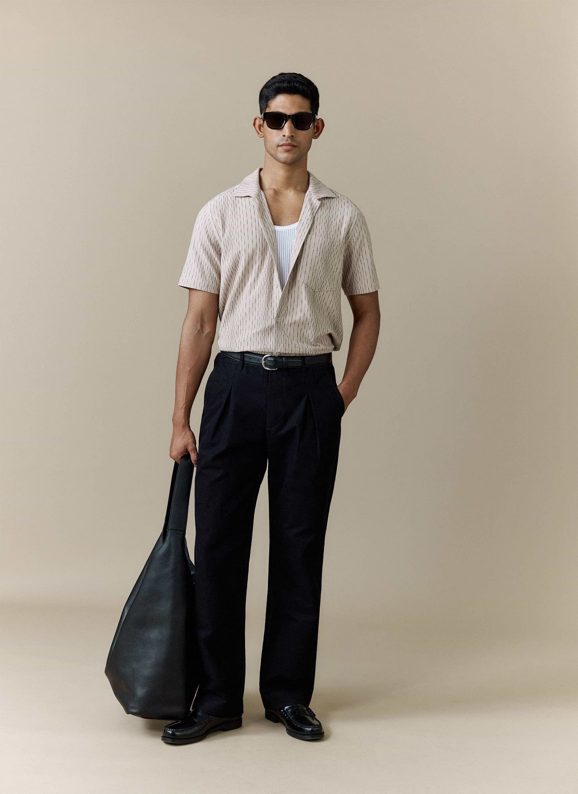 Percival cream cotton Leland Cuban shirt styled with black trousers, a white mesh vest and a black leather tote bag.