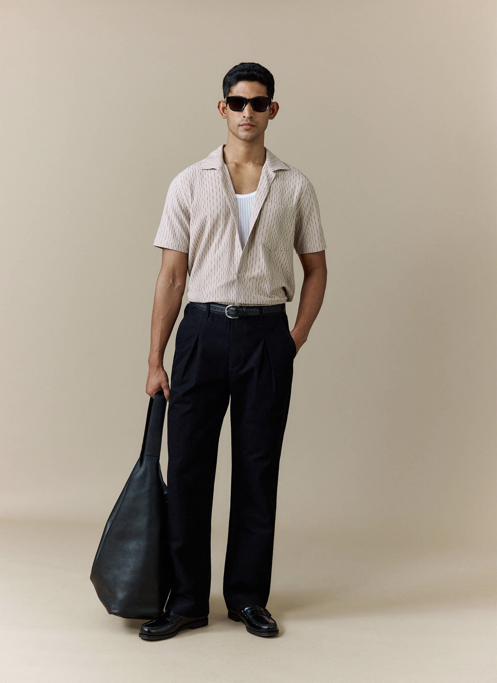 Percival cream cotton Leland Cuban shirt styled with black trousers, a white mesh vest and a black leather tote bag.