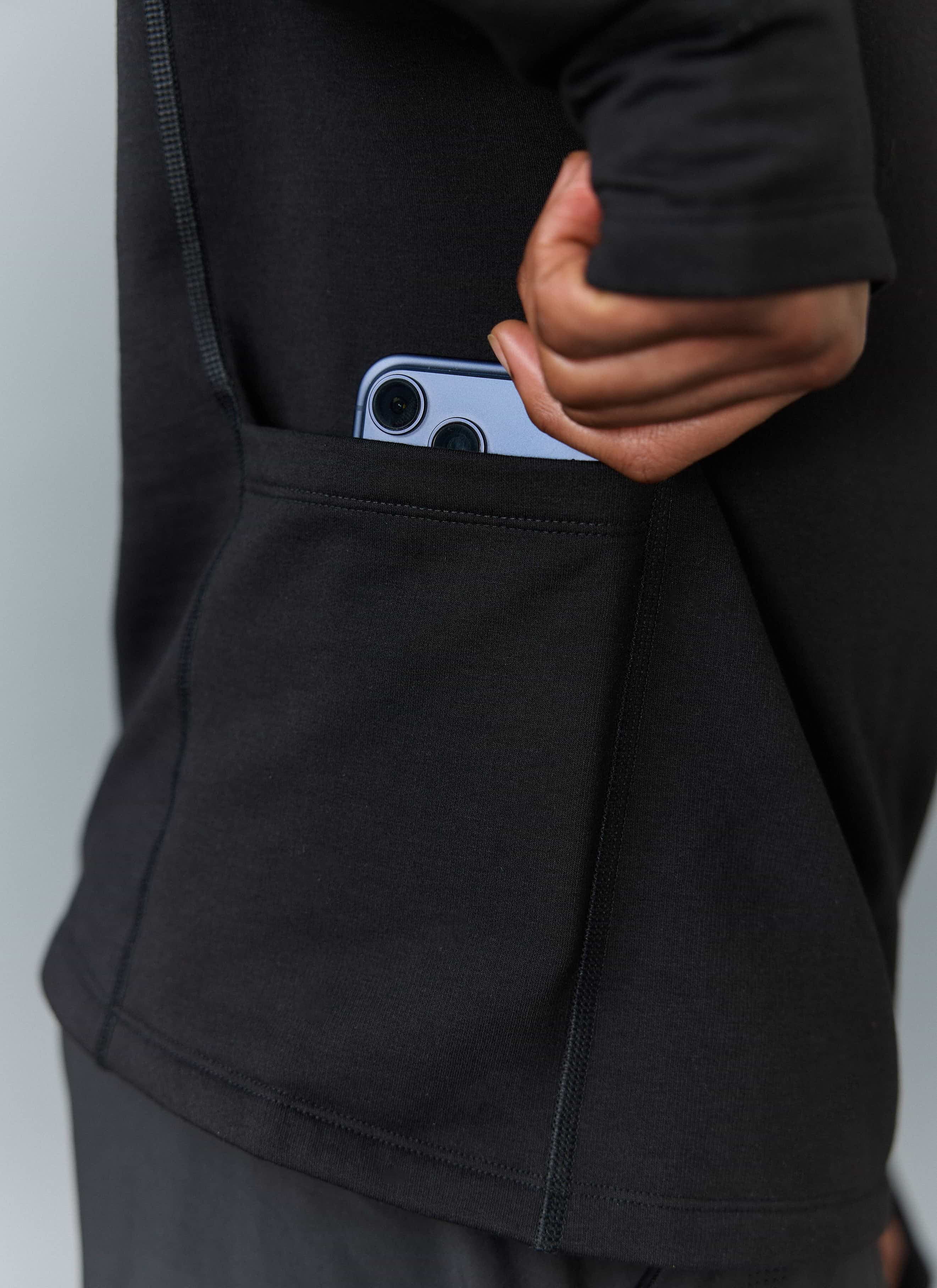 A close-up of the handy low-back stash pocket on the black PCVL Base Layer Quarter Zip Jacket by Percival, holding a phone.