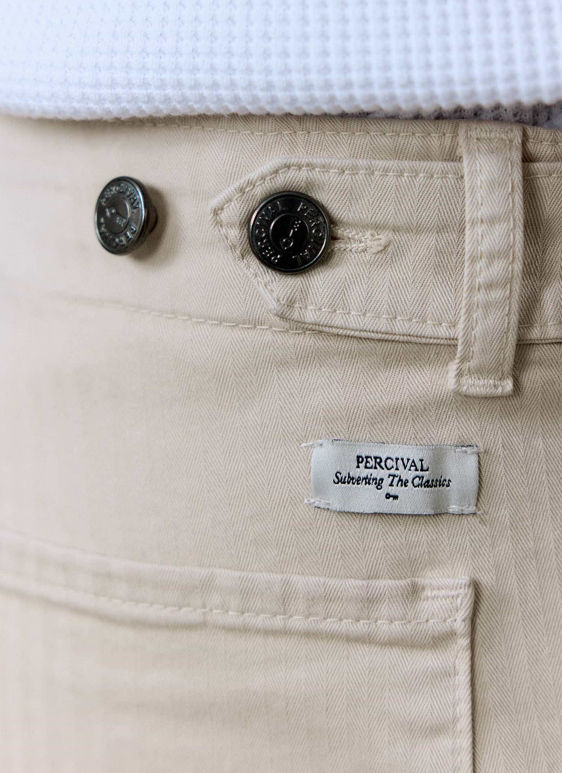 Close-up of the Percival Lungo Herringbone Straight Trousers in ecru, showing the branded buttons and logo label.