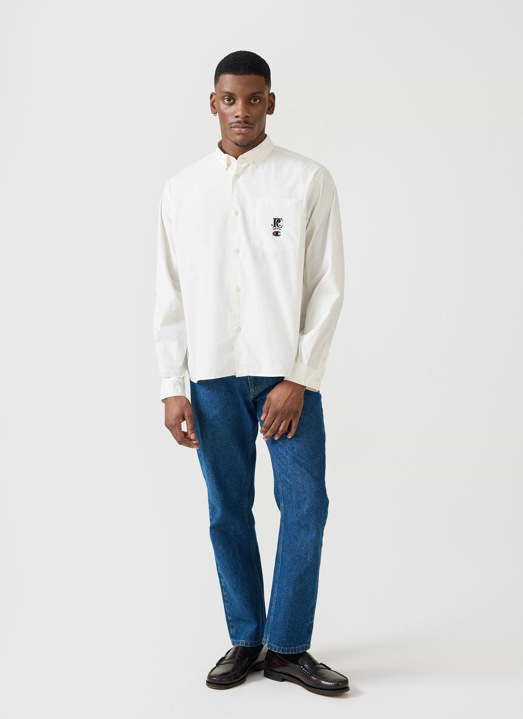 A model wears the ecru Champion x Percival relaxed oxford shirt, styled with blue jeans and loafers.