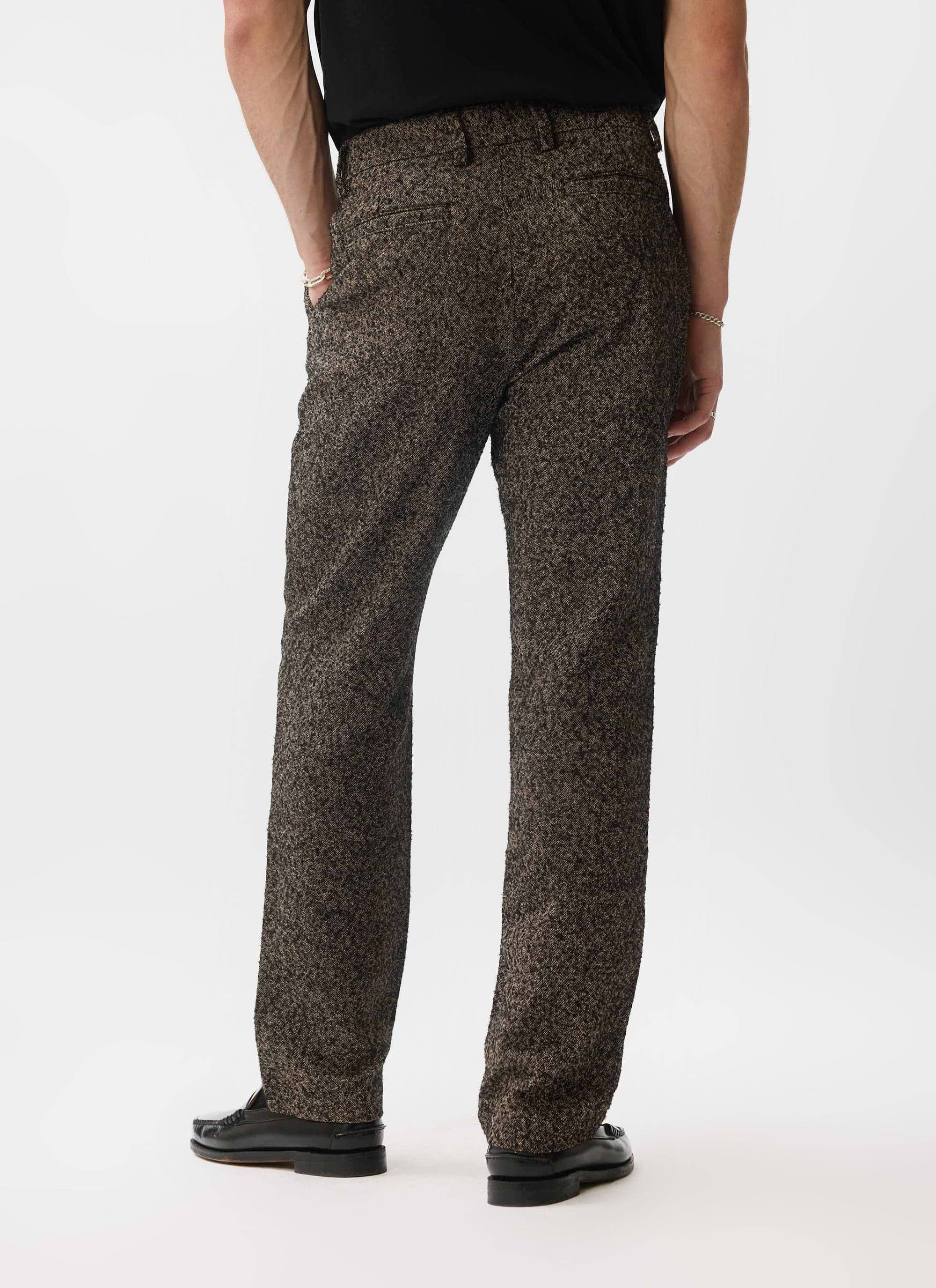 A rear view of a model wearing the Percival Blyton Trousers in a warm grey nep fabric with black loafers.