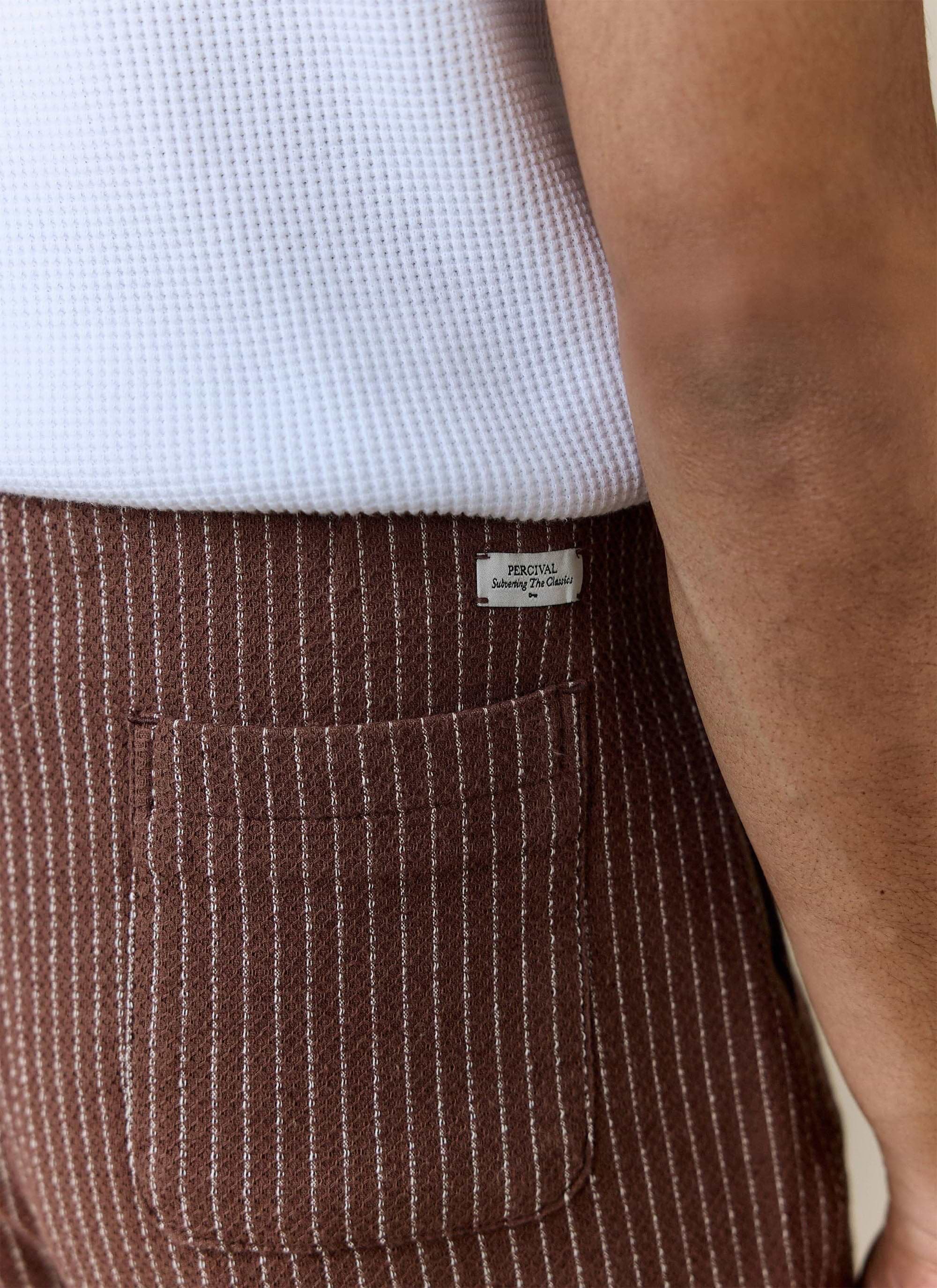 A close-up of a model wearing the brown Sorrento Wide Leg Trousers from Percival, showing the back pocket and brand label.