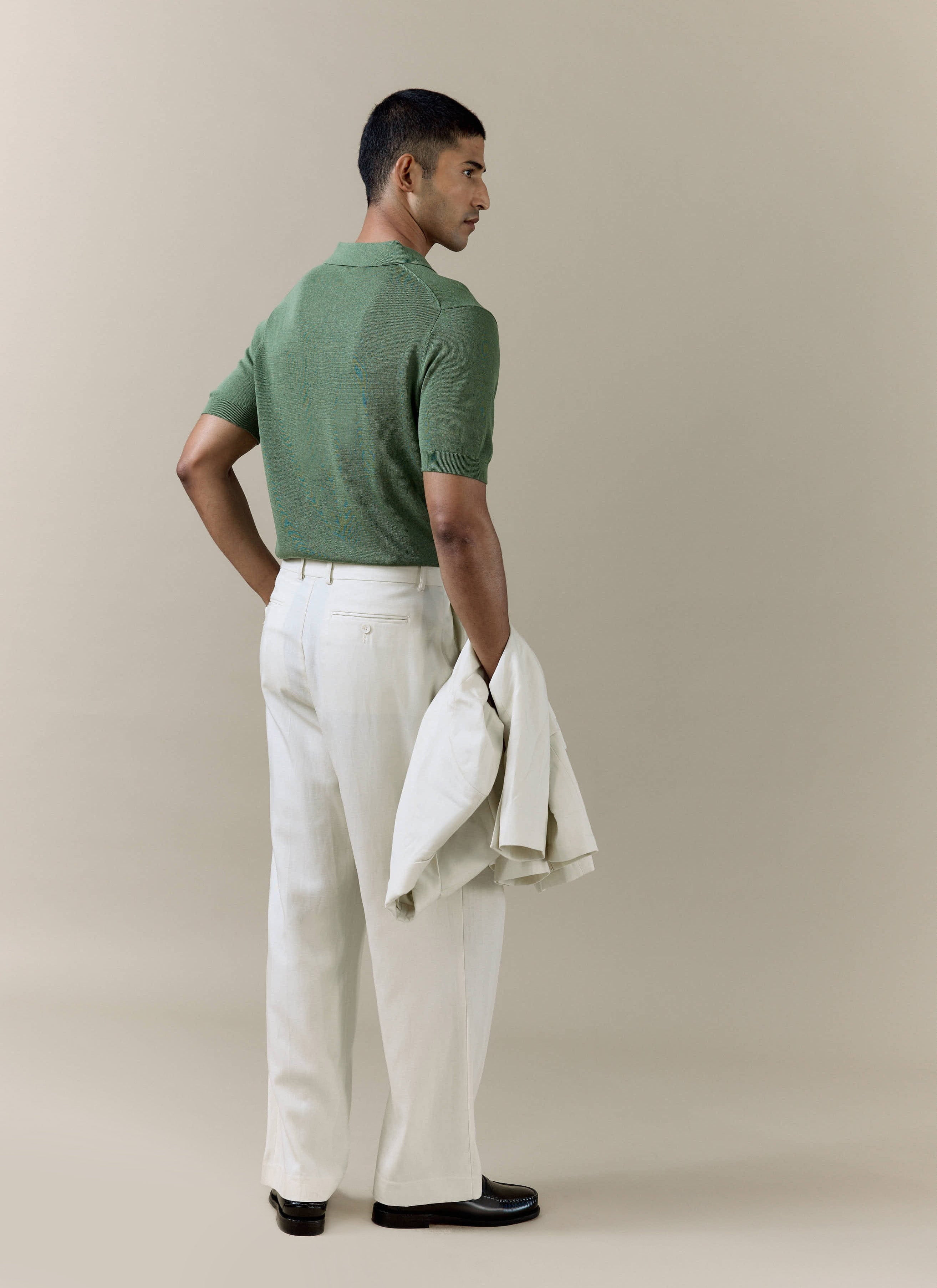 Rear view of a model in the forest green Percival Laurence Knitted Polo, styled with tailored cream trousers.