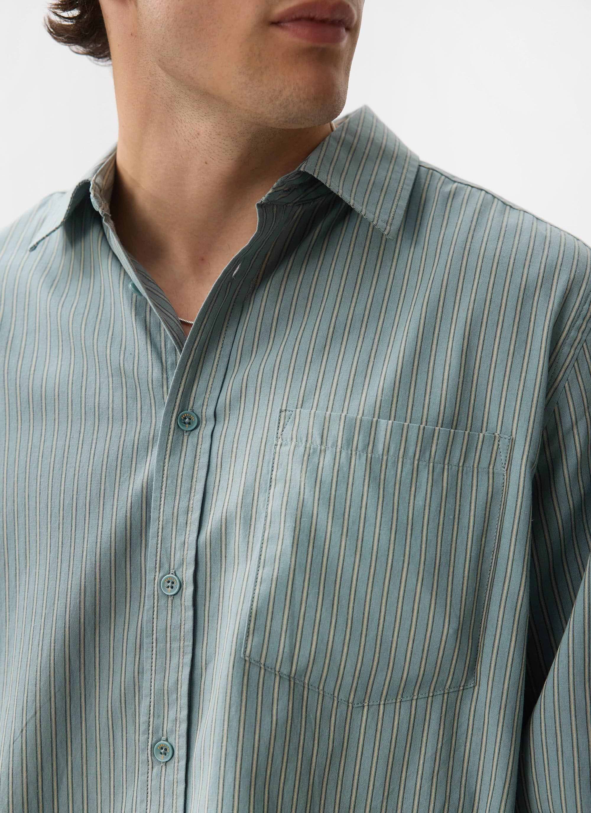 A close-up of a model wearing the Percival Clancy Striped Long Sleeve Shirt in blue, showing the fabric and pocket detail.