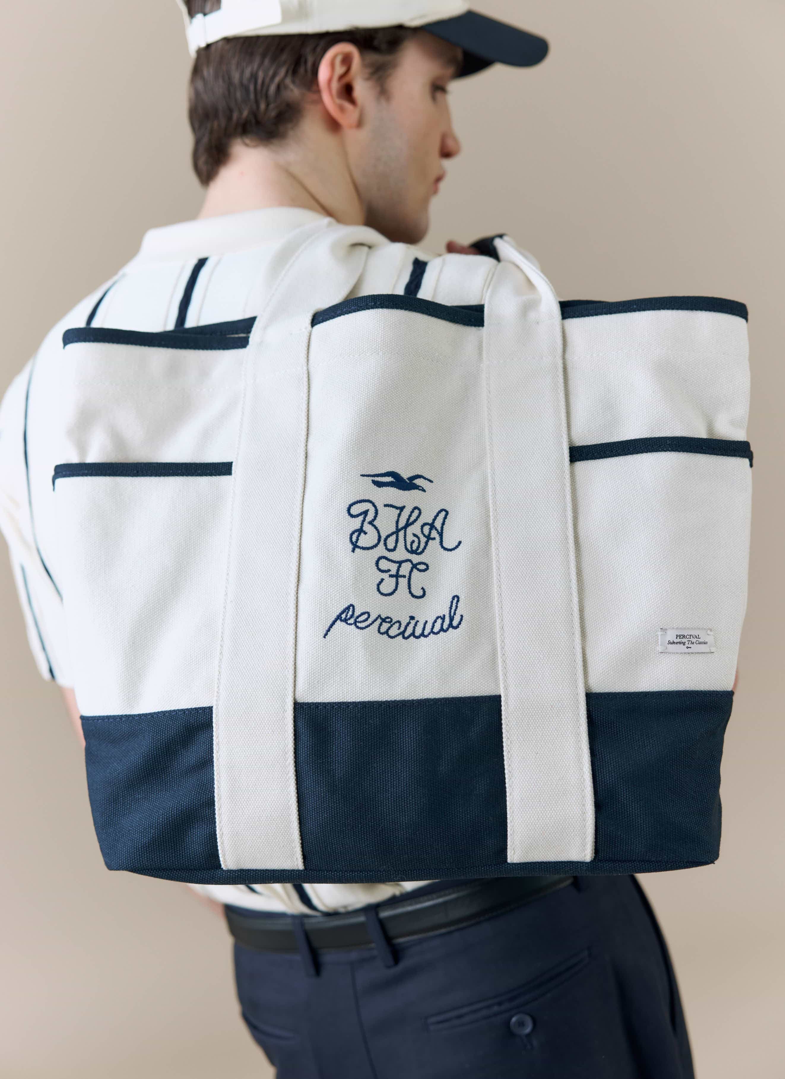 A model viewed from behind carries the Percival x Brighton & Hove Albion F.C. tote bag, showing the navy embroidery detail.