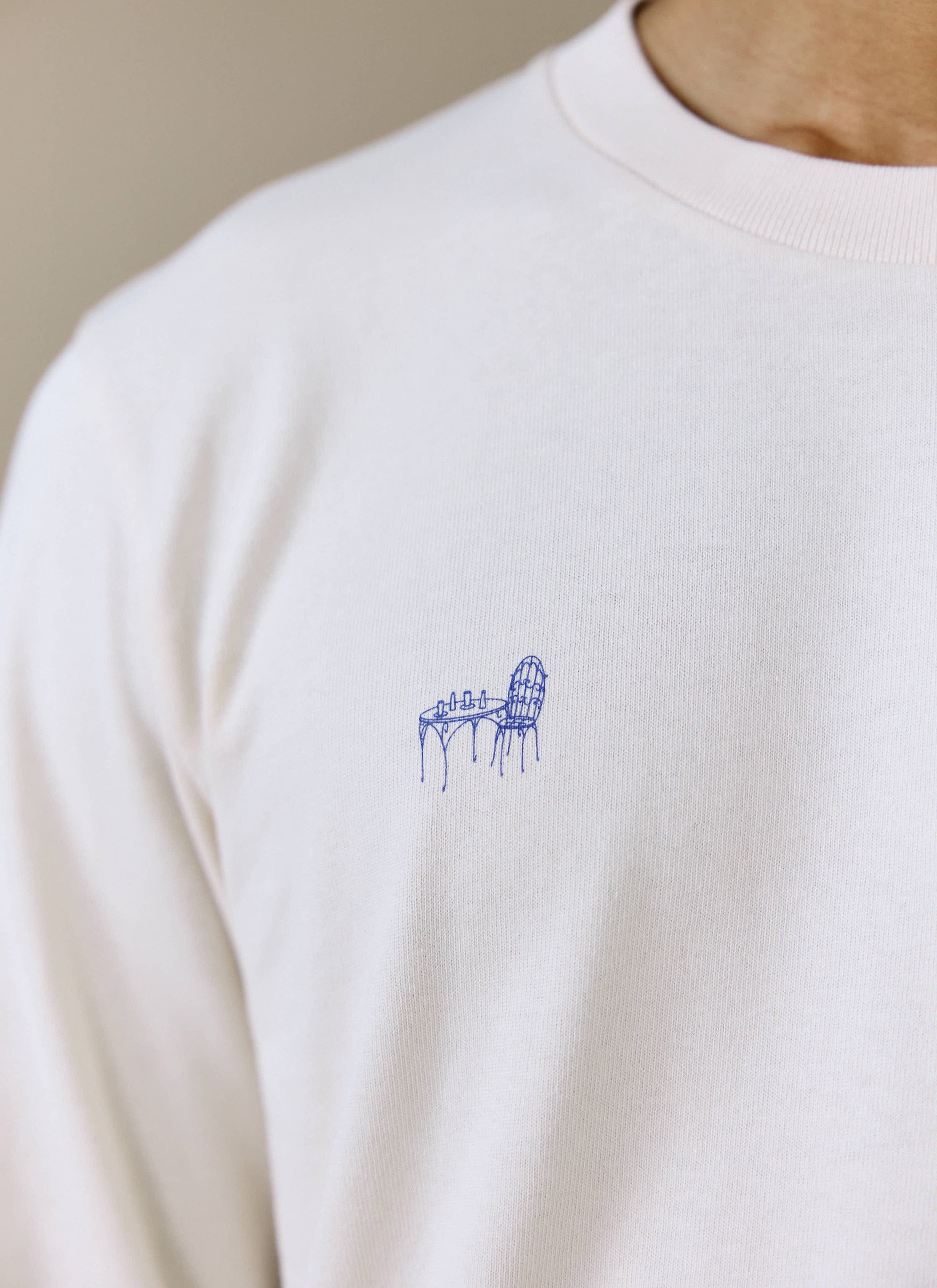A close-up of the blue bistro table graphic on the chest of the Percival Harlow Fine Wines Long Sleeve T Shirt in cream.