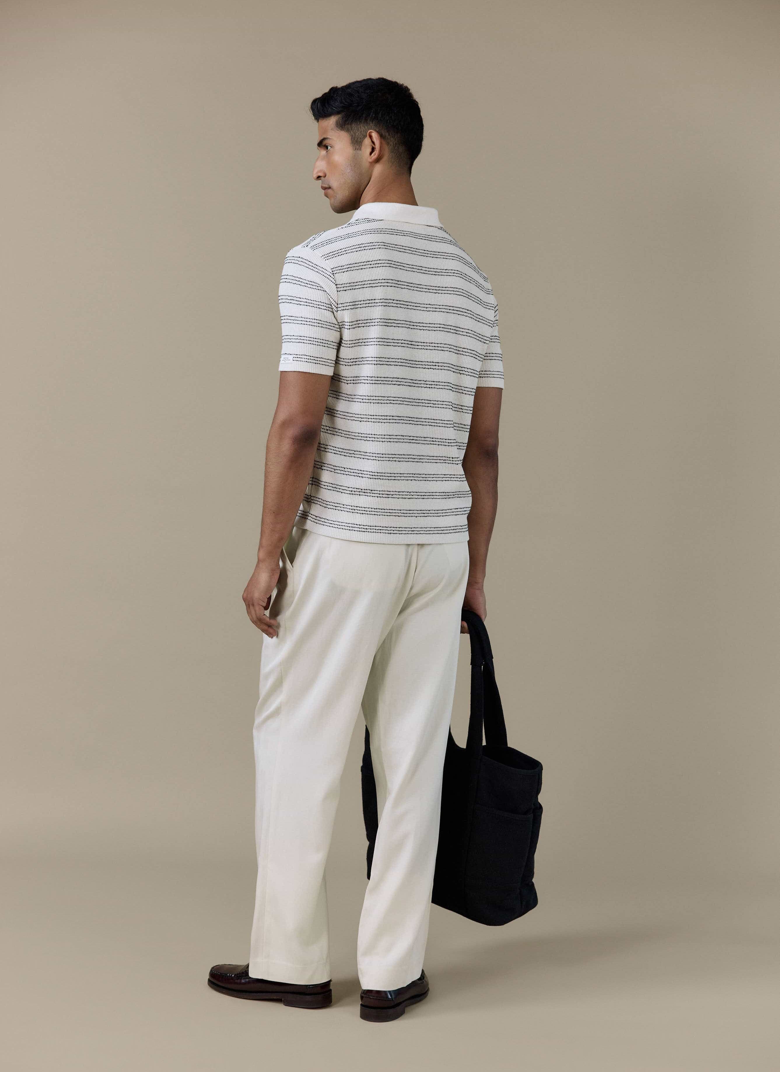Back view of the Percival Laurent Boxy Polo in cream stripe, styled with off-white trousers and a black tote bag.