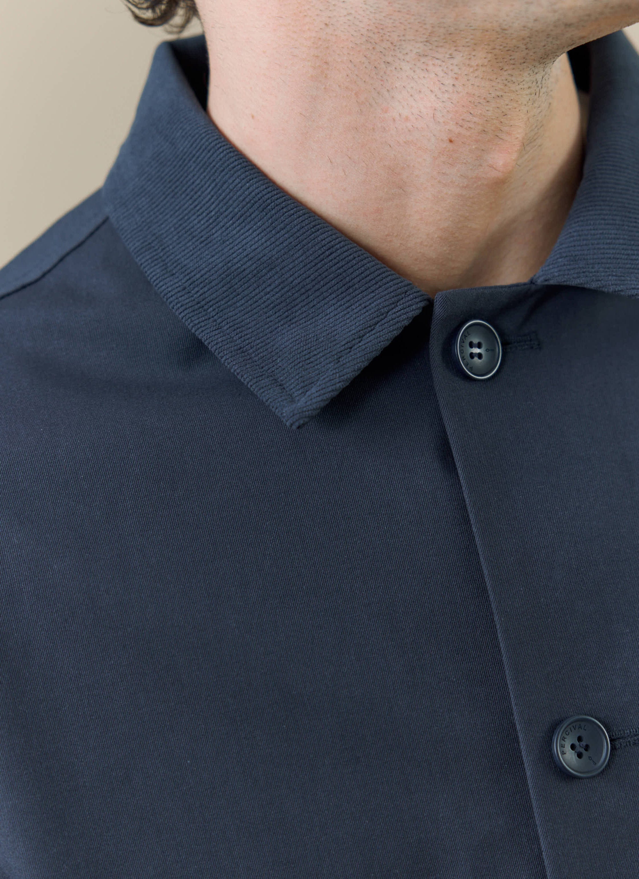 A close-up of the Percival Sherlock Trench in midnight, showing the ribbed collar and branded button detail.