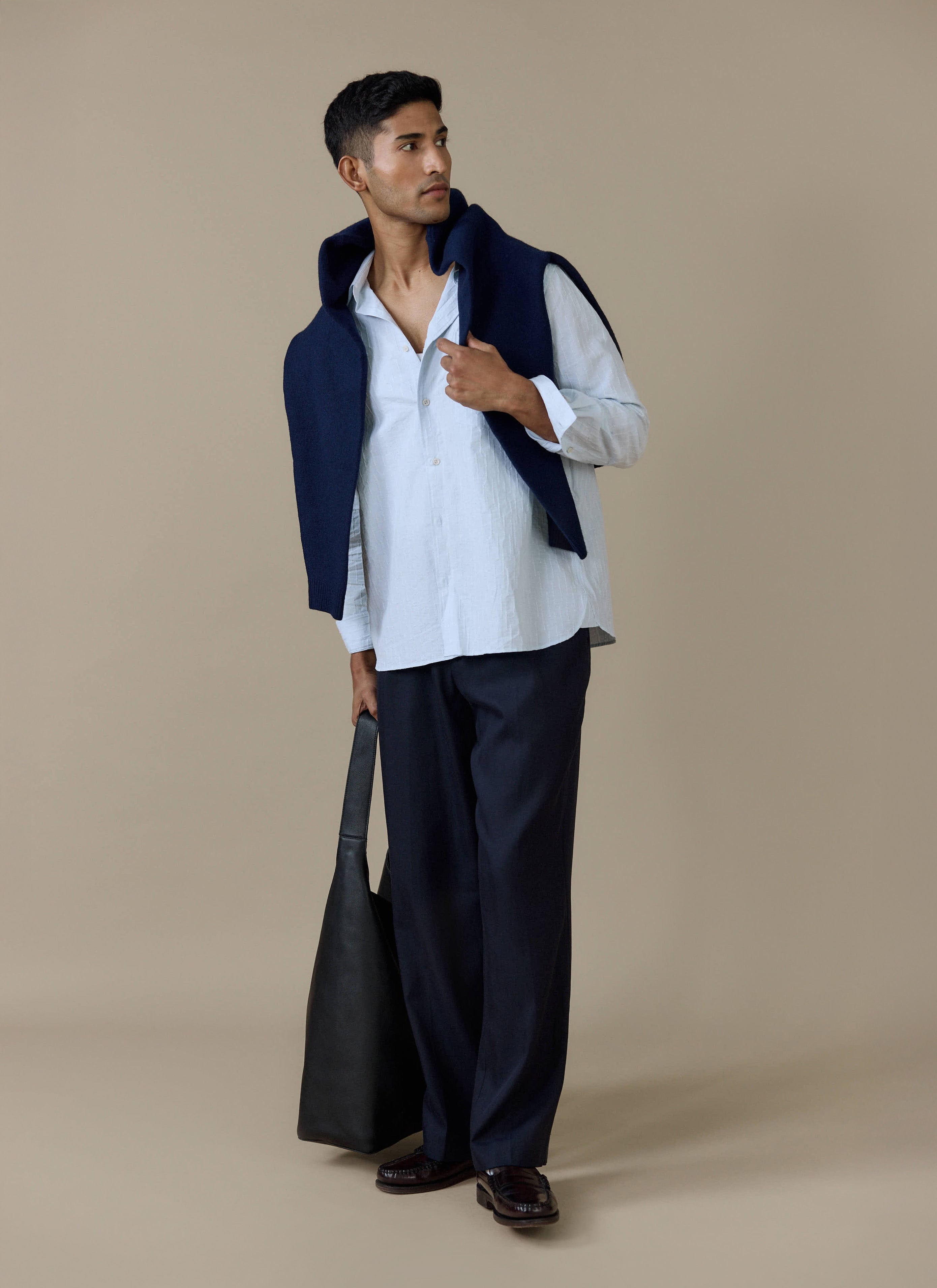 Model wears the light blue Percival Paros Pearce Shirt in seersucker, styled with navy trousers and a navy sweater.