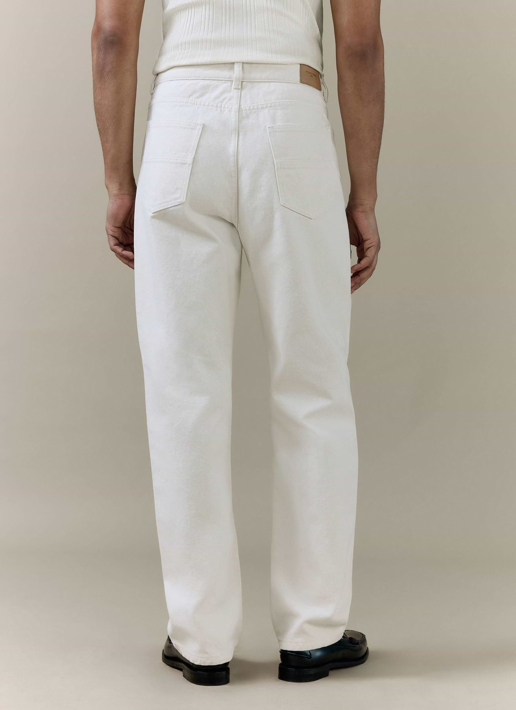 Cream straight leg denim jeans by Percival, shown from the back with two pockets and a tan leather waistband patch.