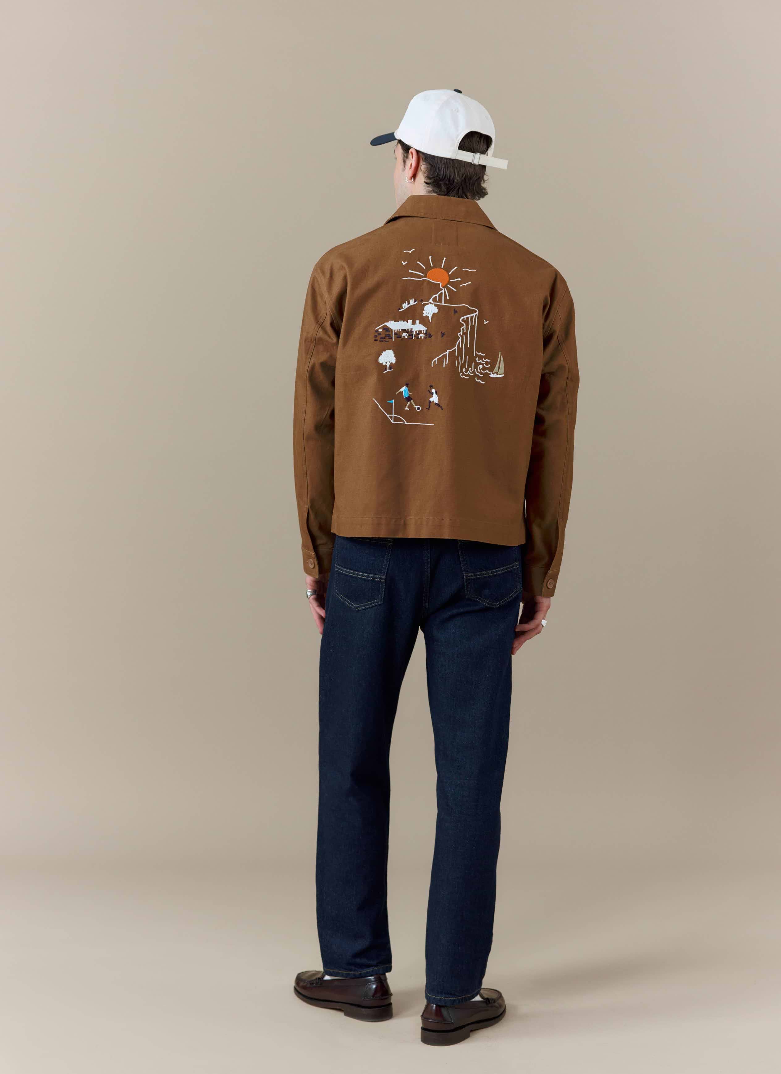 A back view of a model wearing the brown Percival x Brighton & Hove Albion F.C. workshirt with its landscape embroidery.