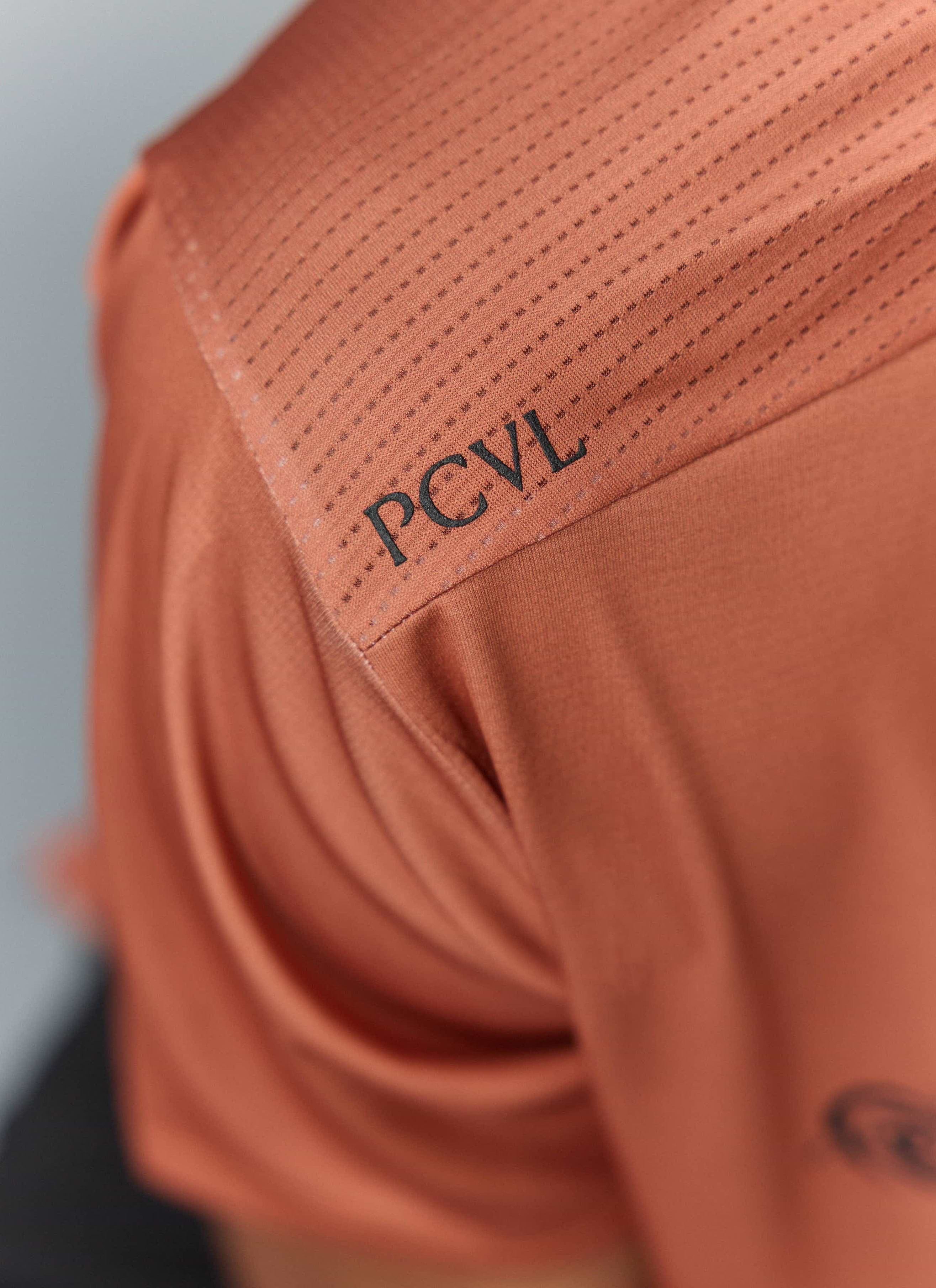 Close-up of the PCVL logo on the shoulder of the rust Percival Printed Performance Top, showing the breathable fabric detail.