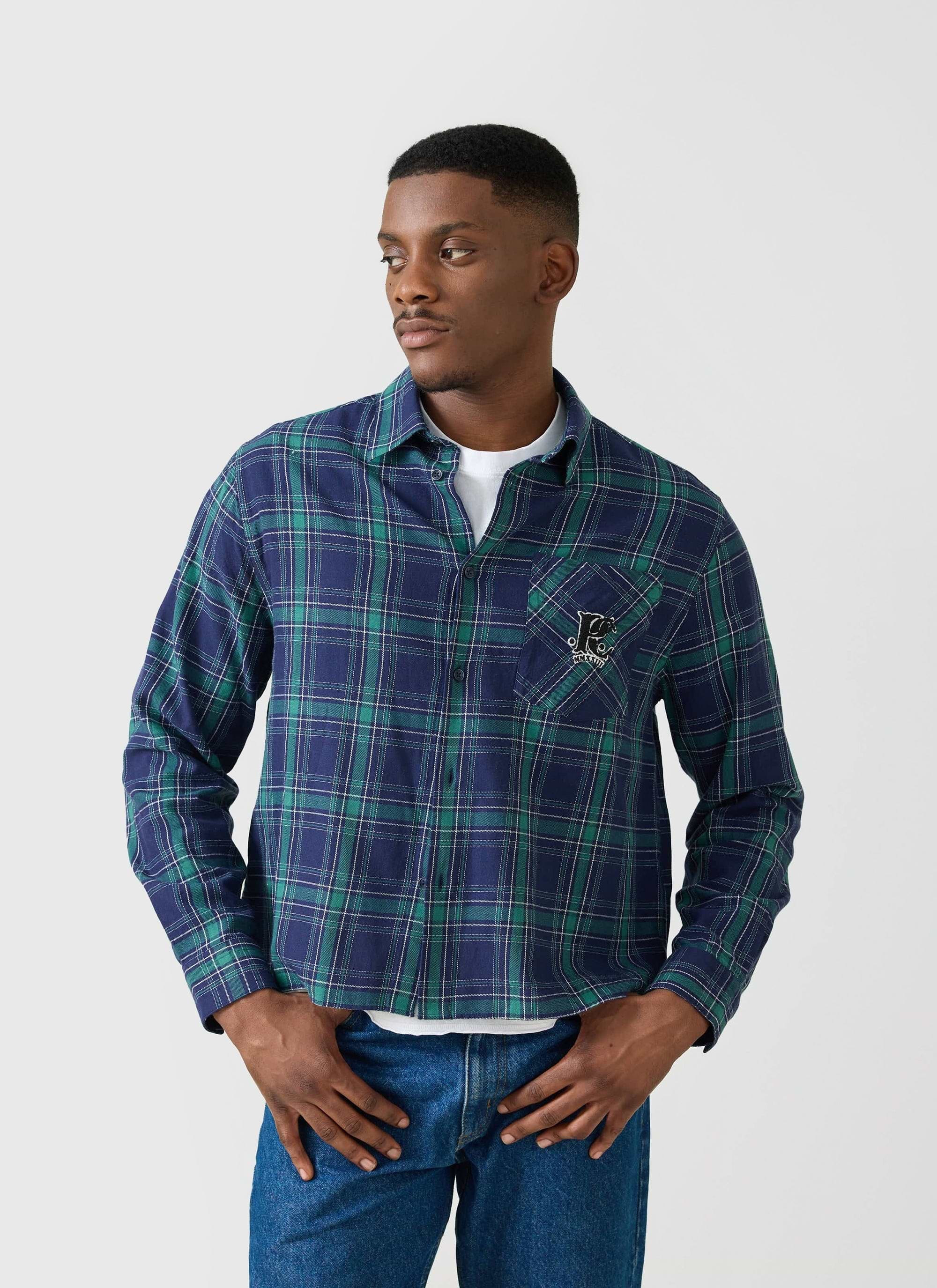 A model wears the Champion x Percival check long sleeve shirt in a blue and green tartan, styled open over a white t-shirt.