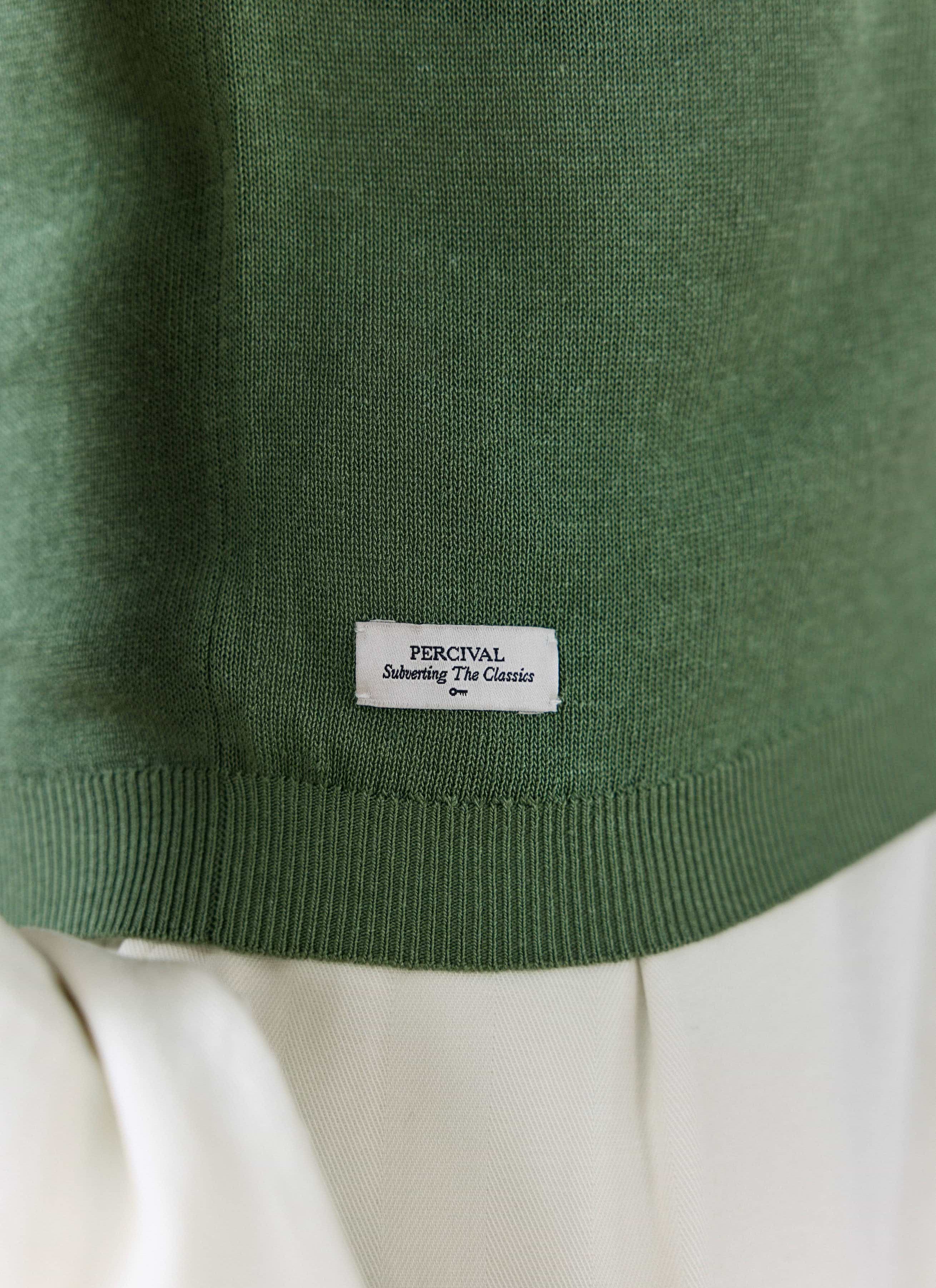 Close-up of the forest green Laurence Knitted Polo by Percival, highlighting the ribbed hem and white logo tag.
