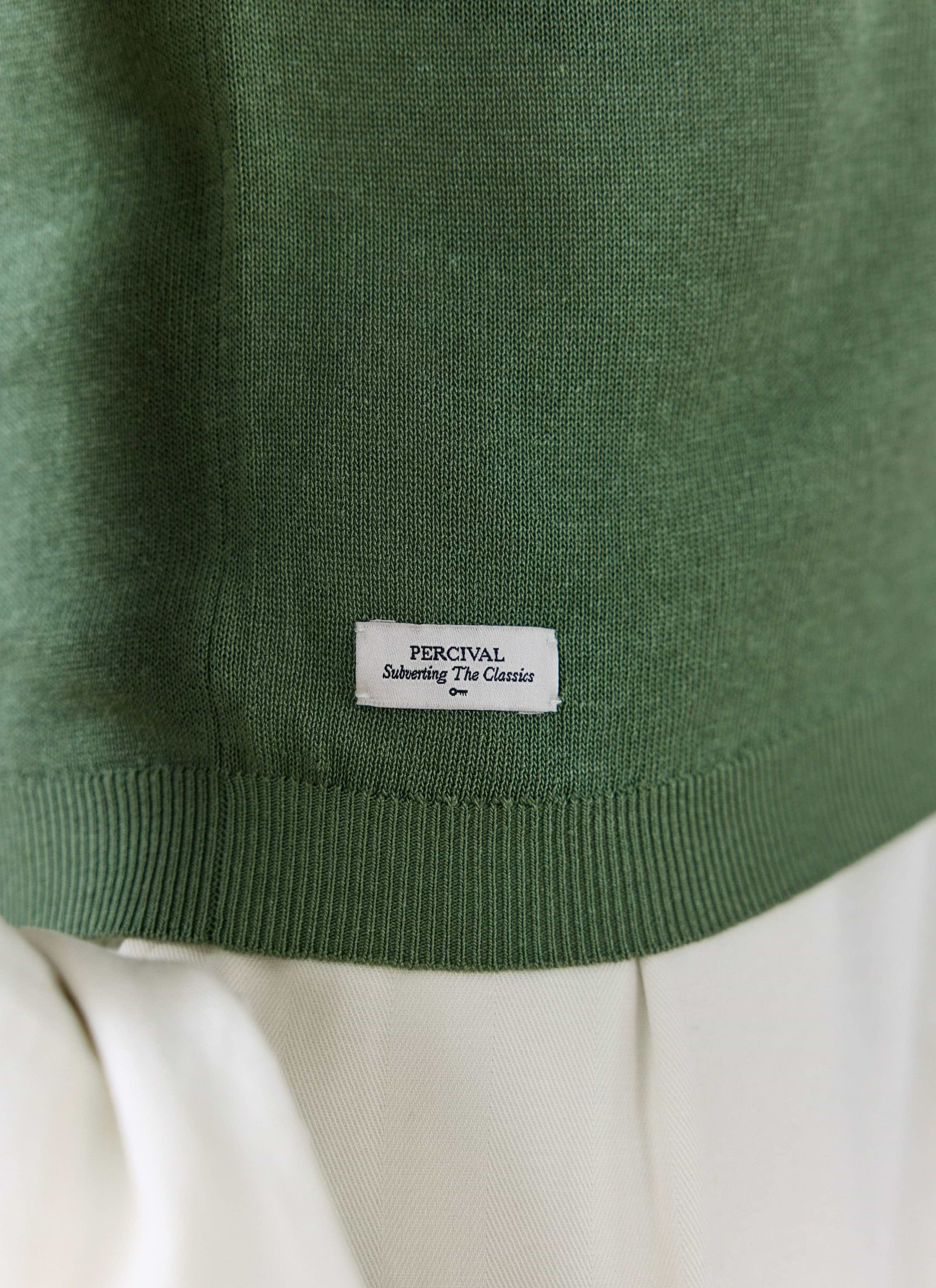 Close-up of the forest green Laurence Knitted Polo by Percival, highlighting the ribbed hem and white logo tag.