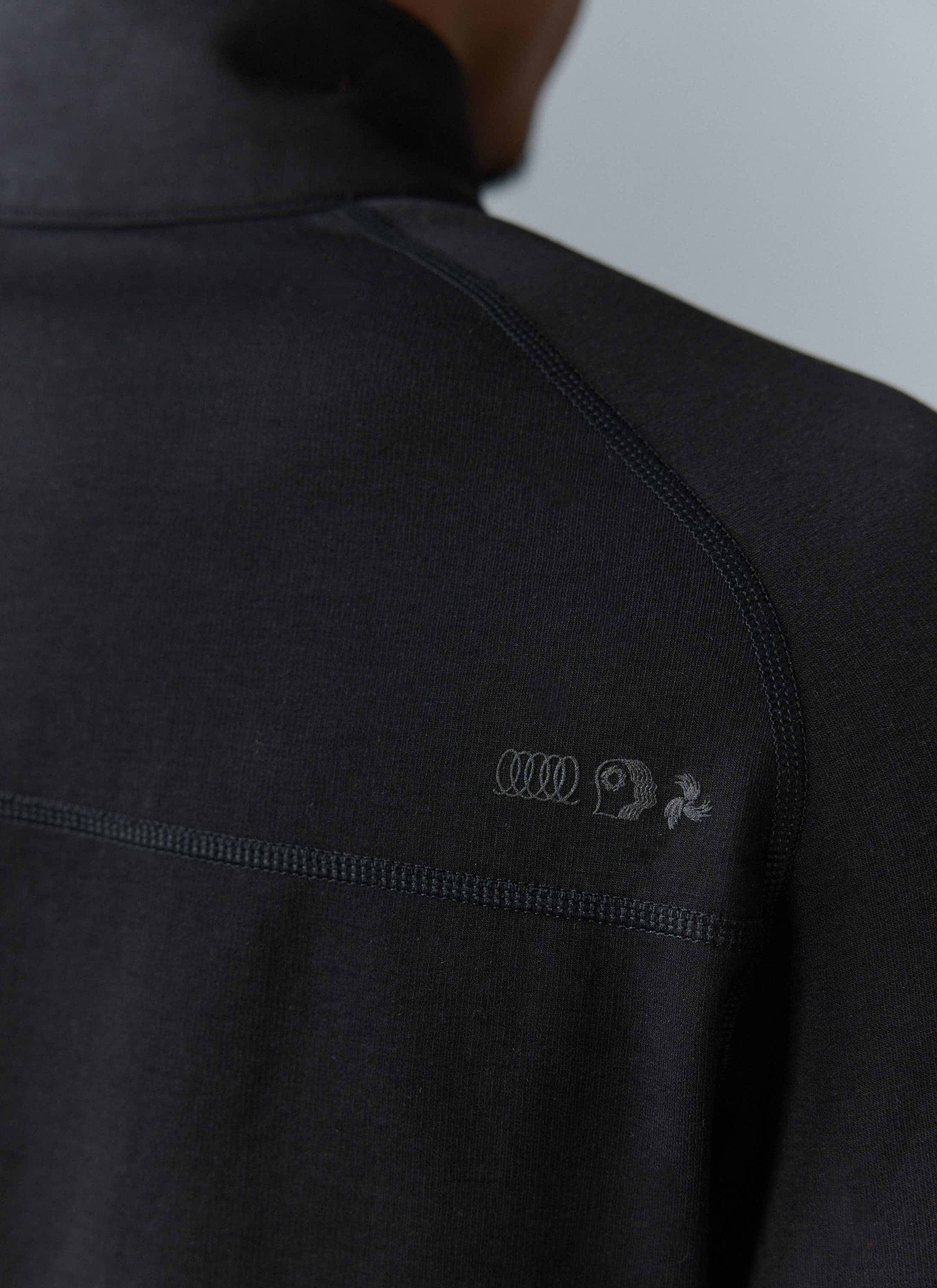 Close-up of the Percival PCVL Base Layer Quarter Zip in black, showing the tonal chest logo and flatlock seam detail.