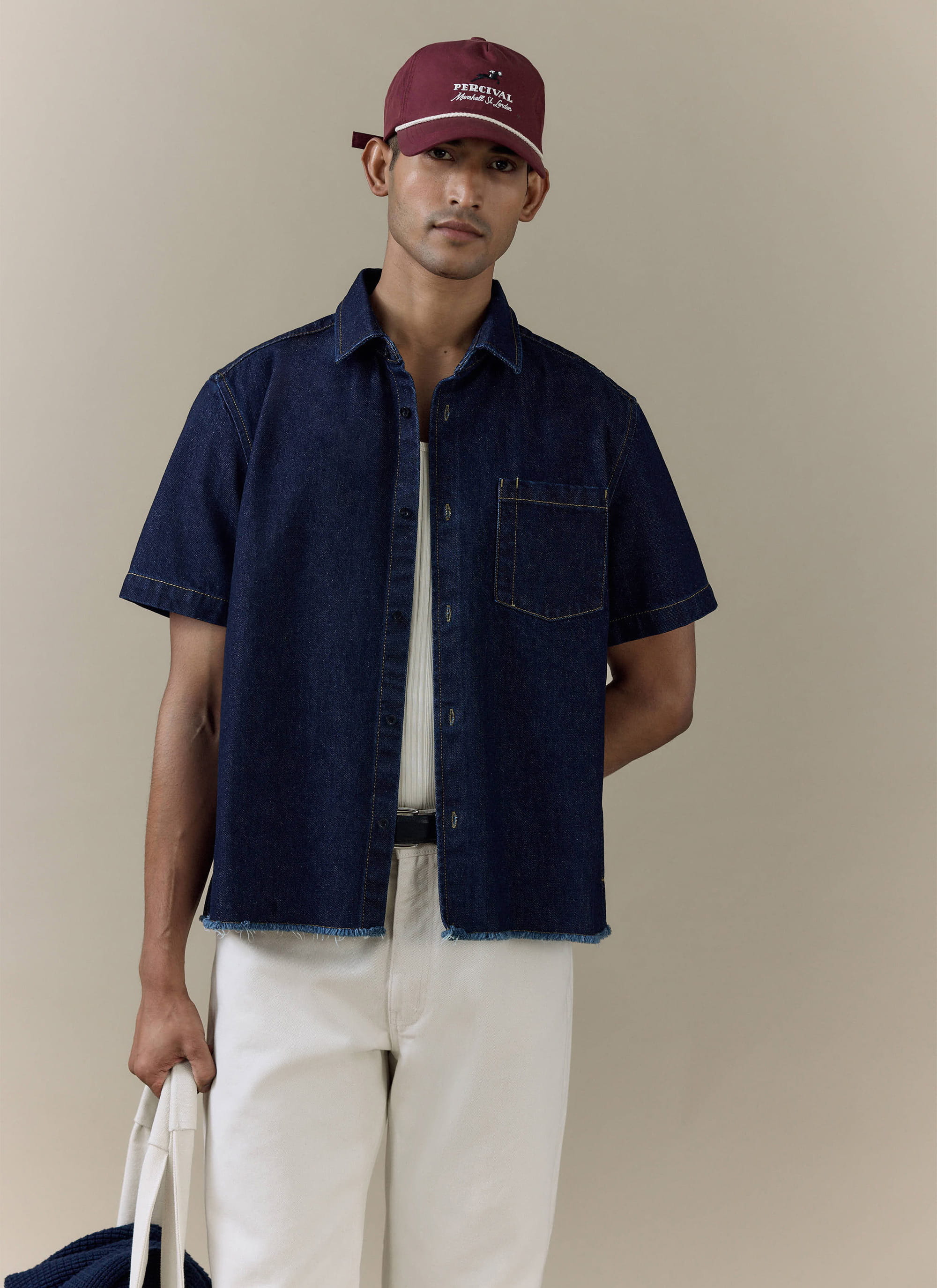 Model wearing the Percival Harley Denim Cropped Boxy Shirt in dark indigo cotton, featuring a raw, frayed hem.