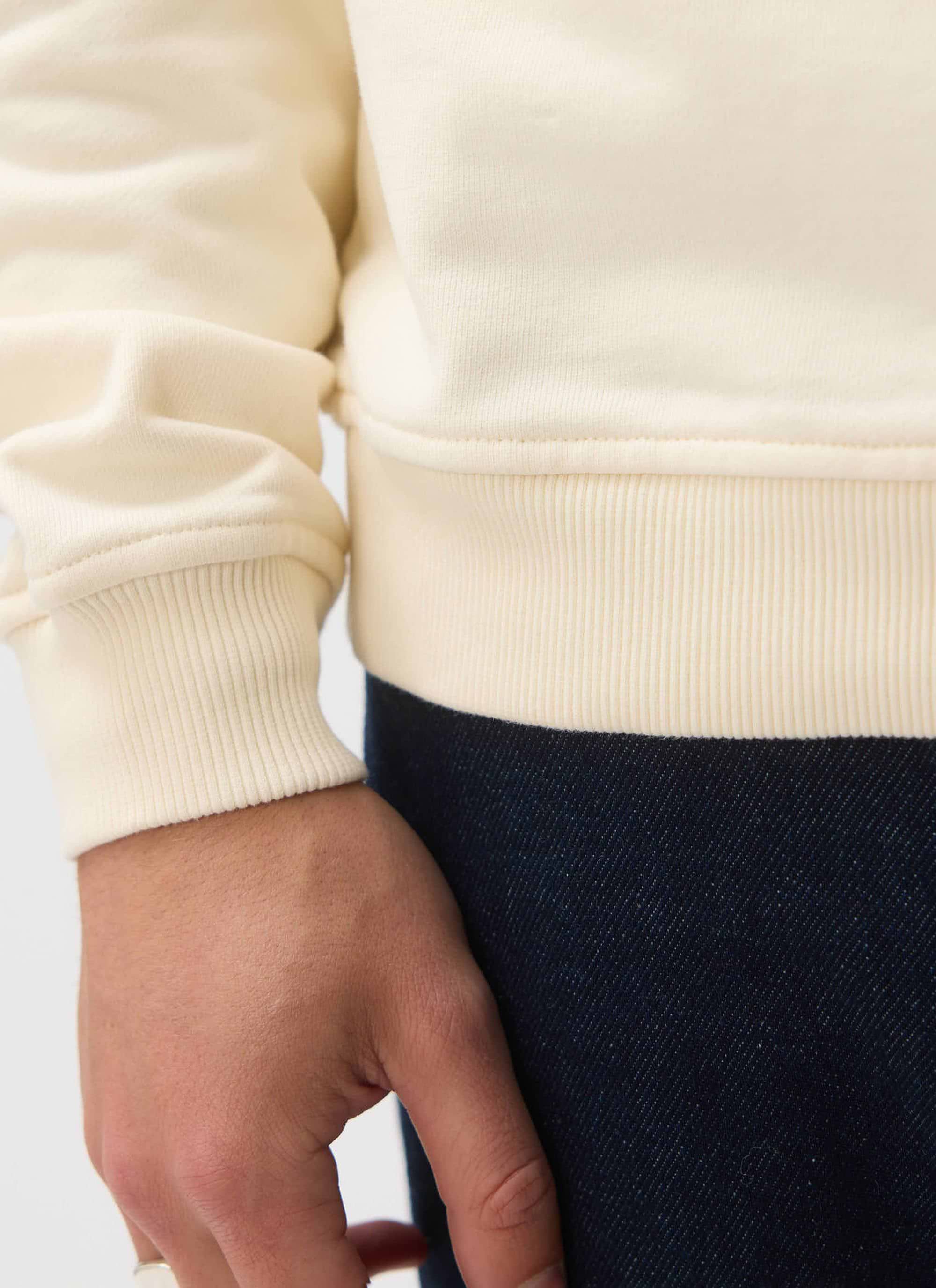 A close-up of the ribbed hem and cuff detail on the Percival Bistro Printed Sweatshirt in ecru organic cotton.
