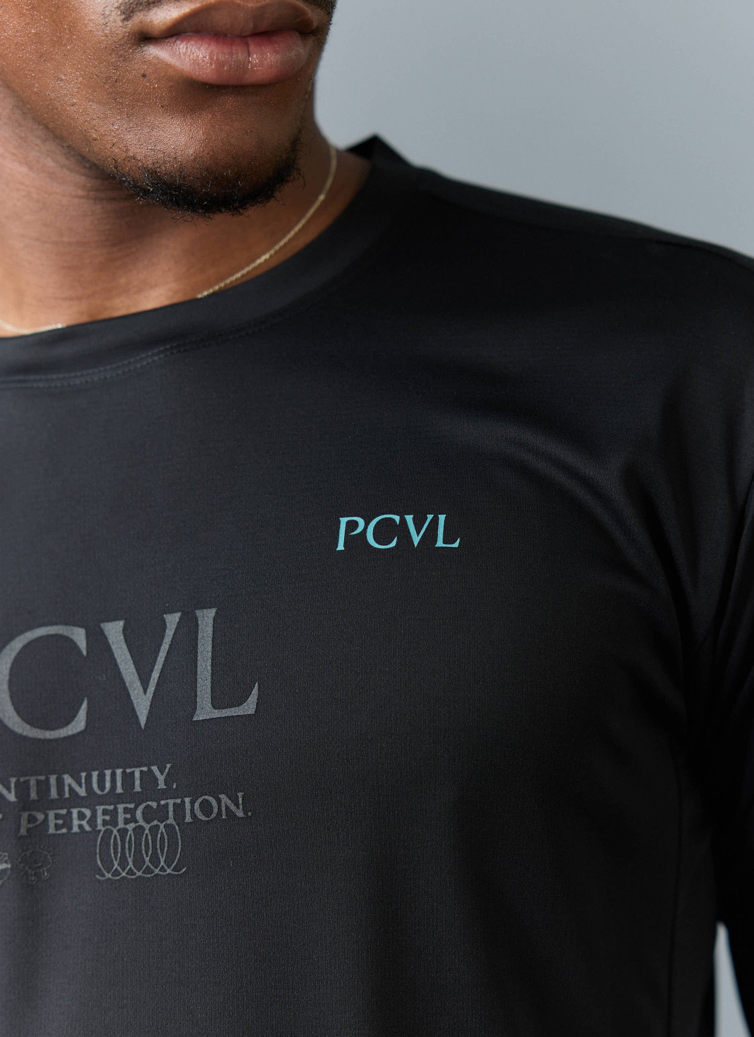 A close-up of the Percival PCVL Long Sleeve Printed Performance Top in black, detailing the teal and tonal chest graphics.