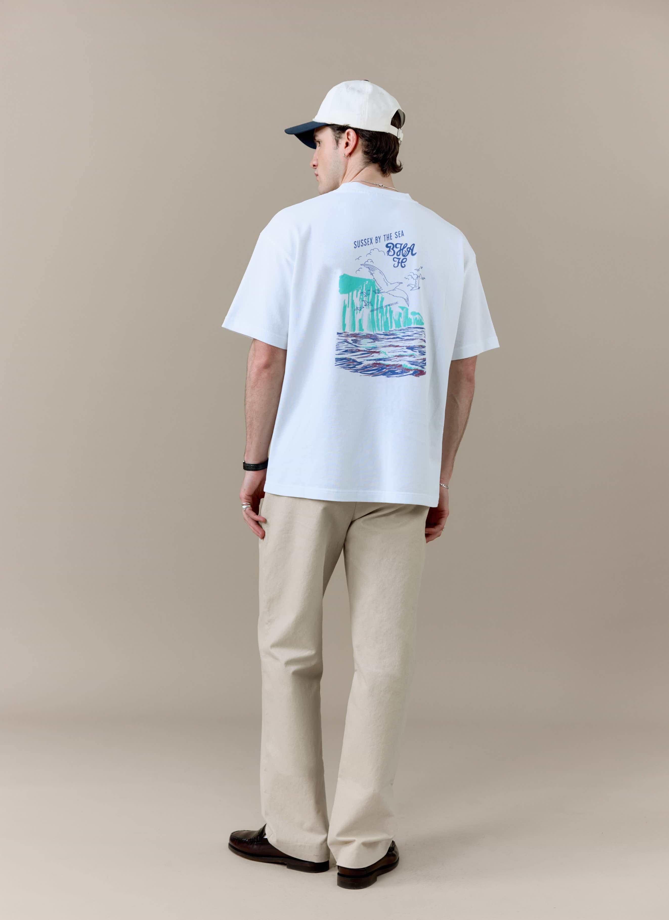 A model from behind wearing the white Percival x Brighton & Hove Albion F.C. t-shirt, showing the colourful back print.