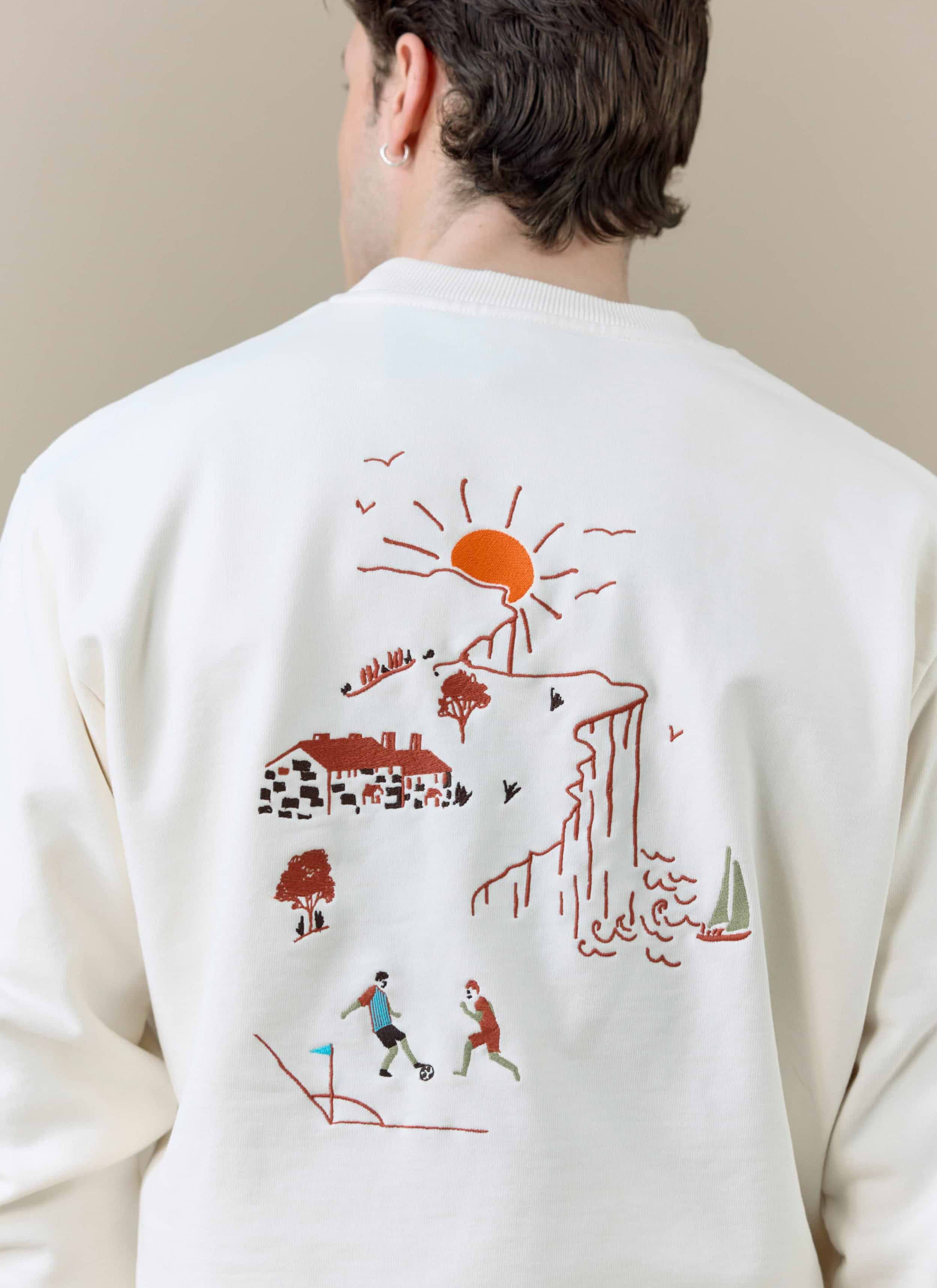 A close-up of the embroidered seaside and football scene on the back of cream Percival x Brighton & Hove Albion sweatshirt.