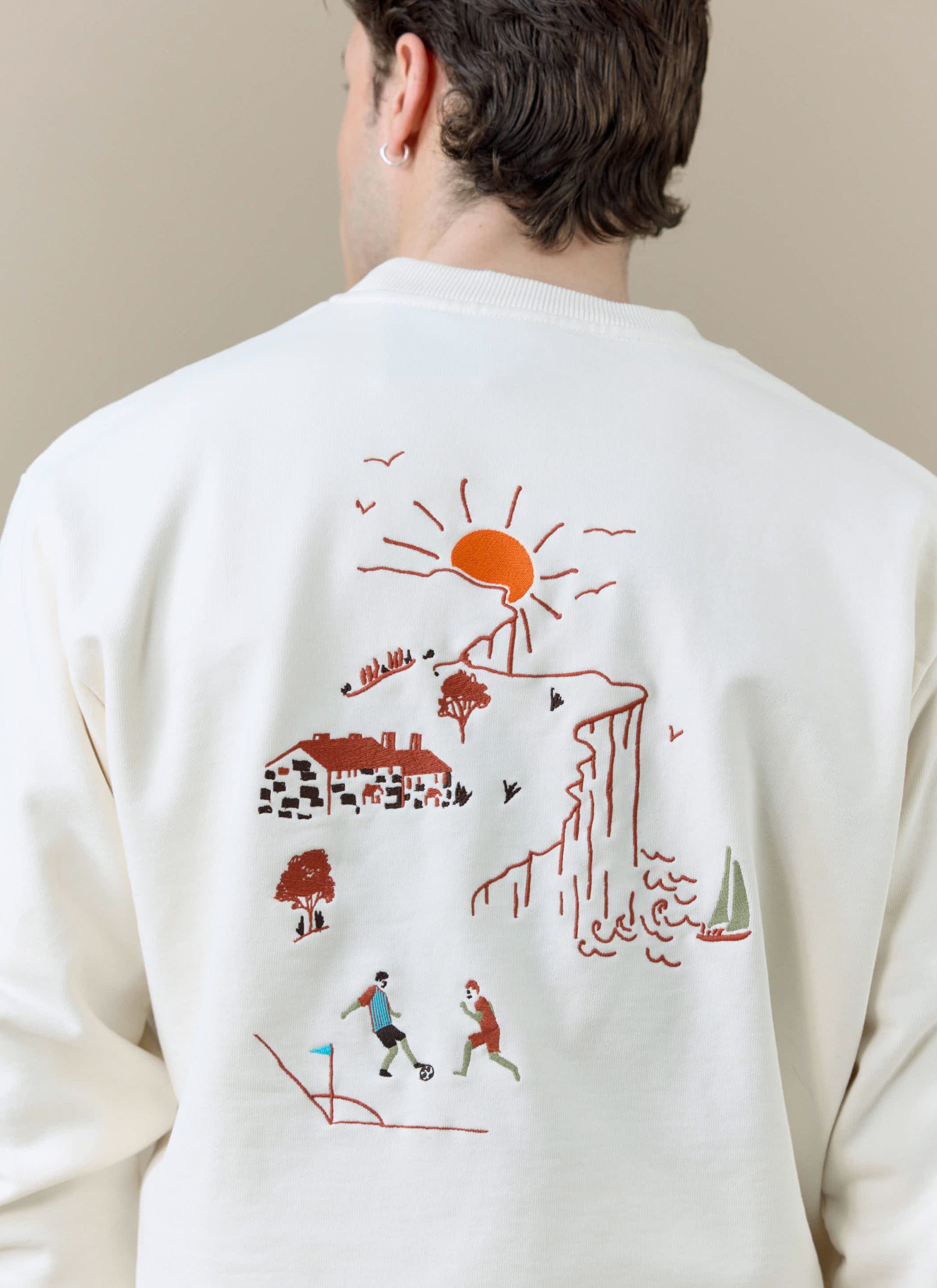 A close-up of the embroidered seaside and football scene on the back of cream Percival x Brighton & Hove Albion sweatshirt.