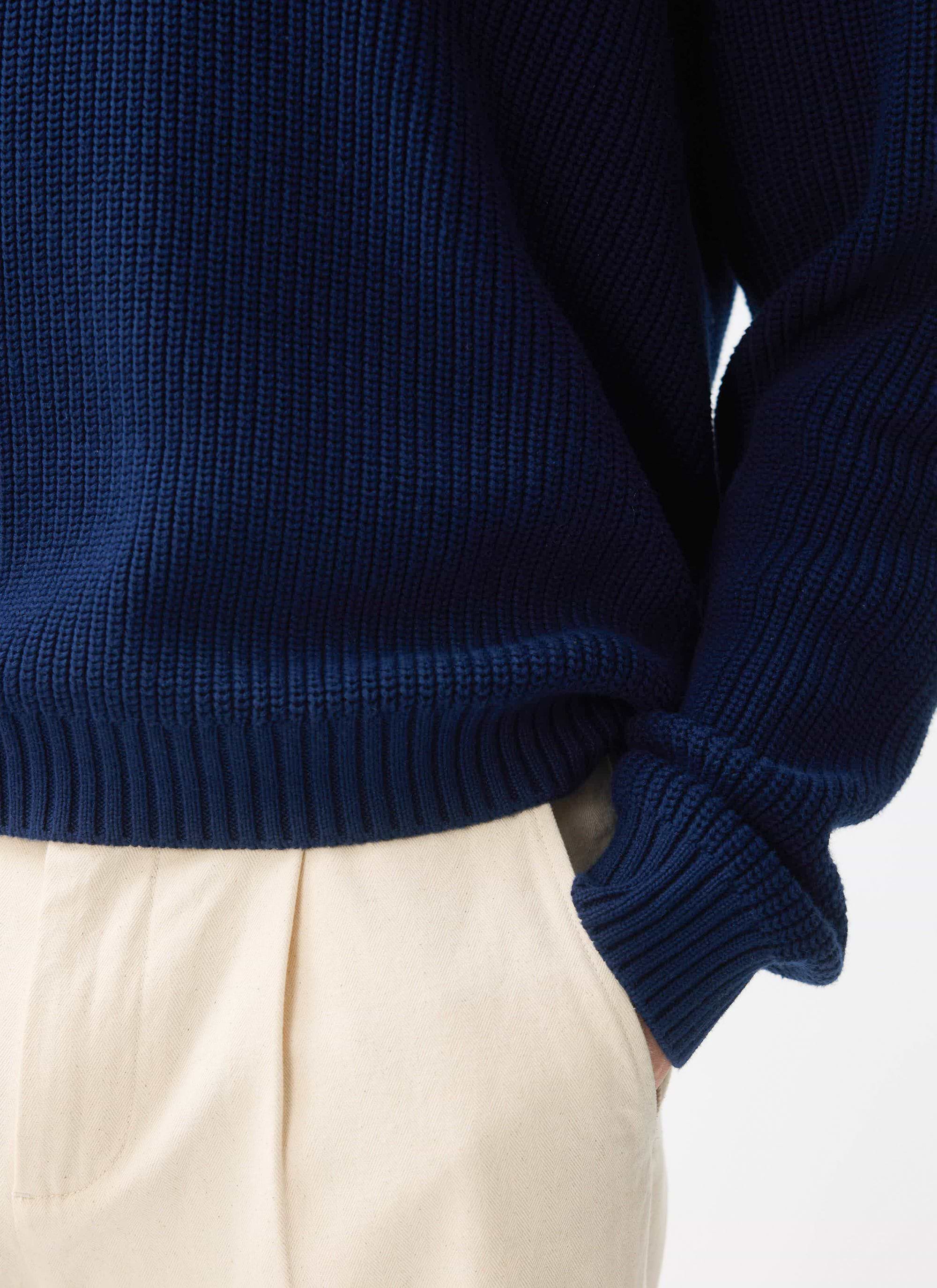 A close-up of the Percival Meyer Quarter Zip jumper in blue, showing the chunky cotton knit, worn with cream trousers.