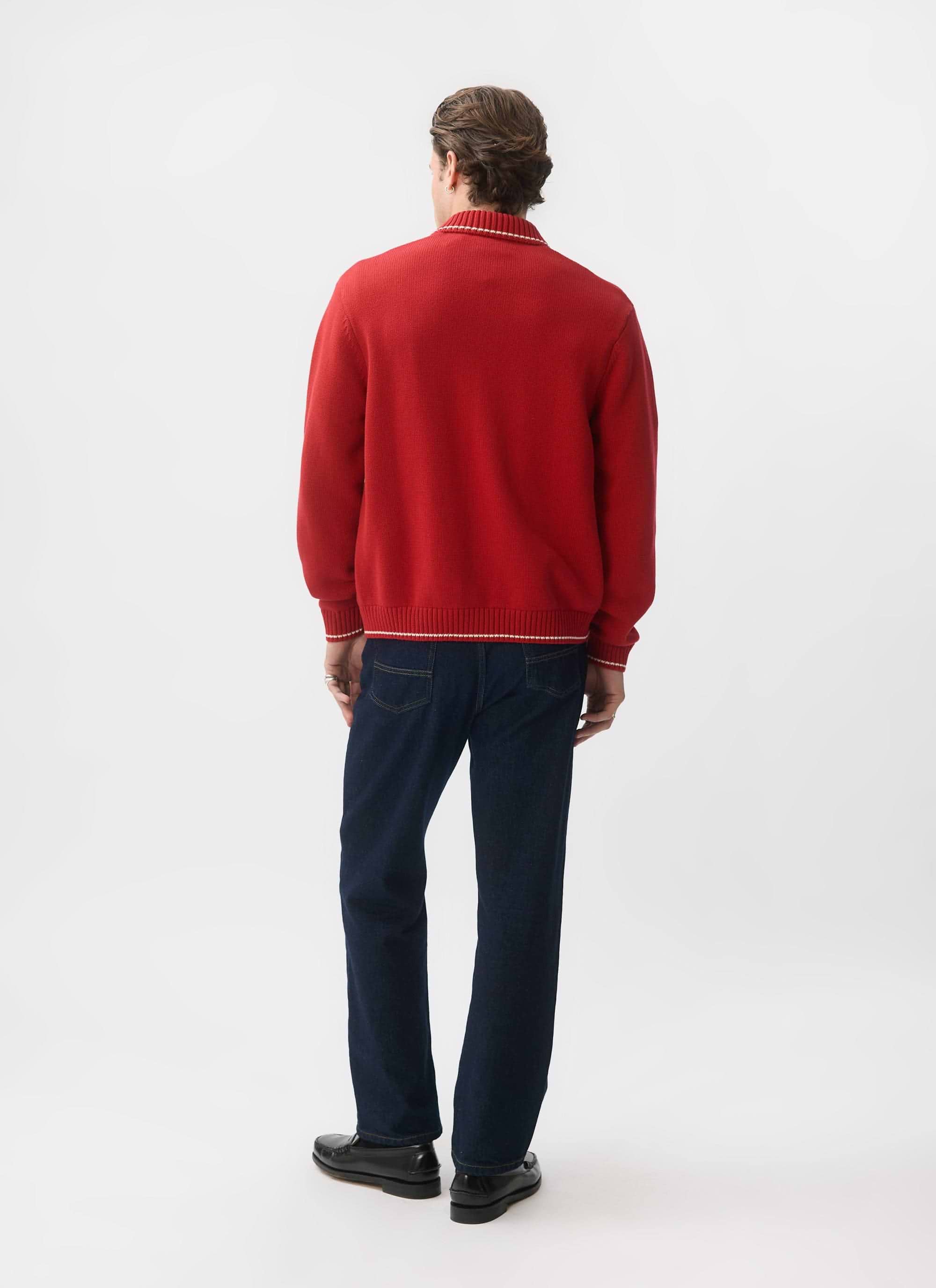 A model, seen from behind, wears the Percival Gardner Dense Knitted Zip Cardigan in red with dark jeans and loafers.