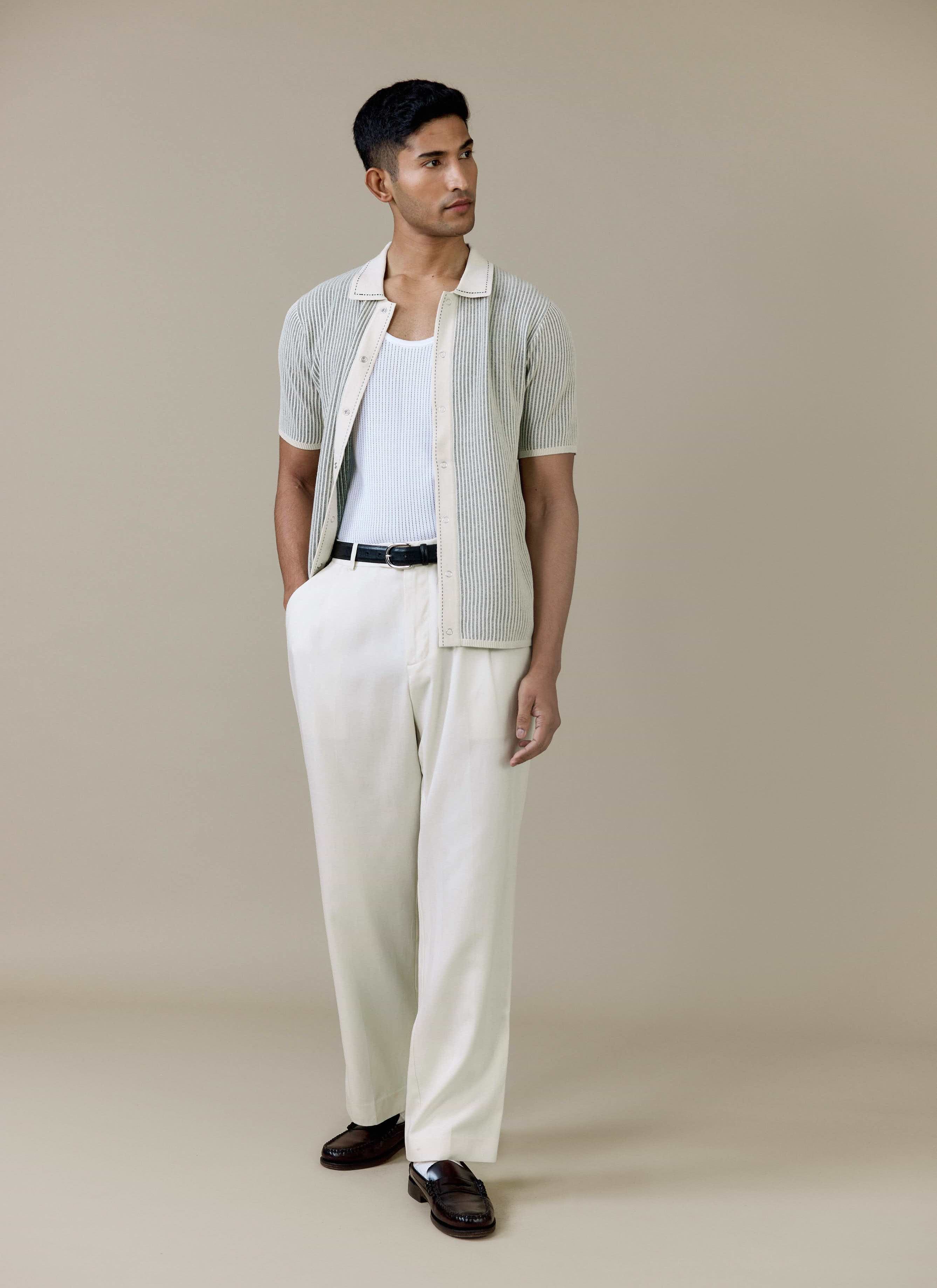 Model wears the cream Dixon Knitted Shirt from Percival, styled open with a white vest and off-white trousers.