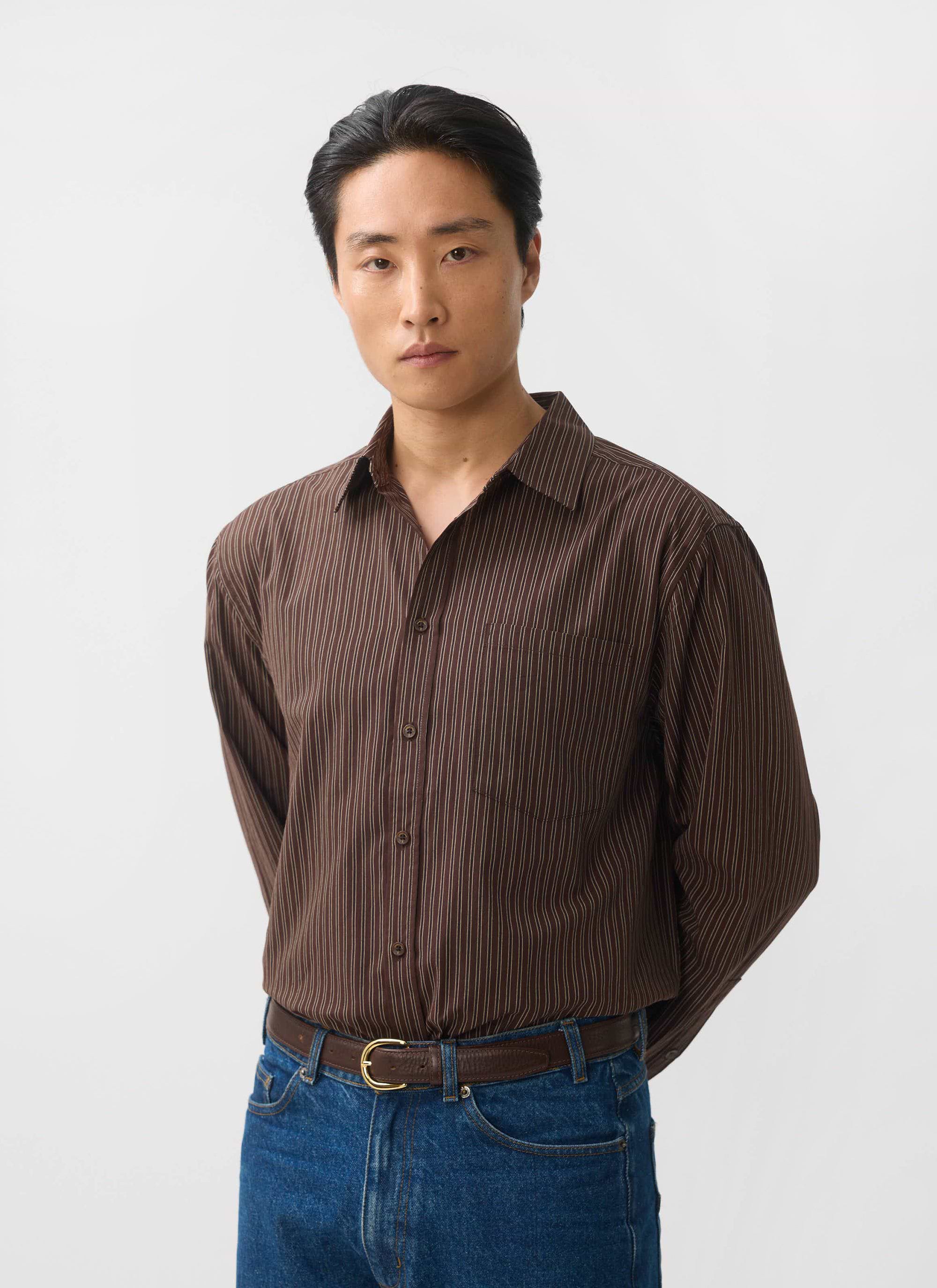 A model wears the Percival Clancy Striped Long Sleeve Shirt in brown, styled with blue jeans against a white background.