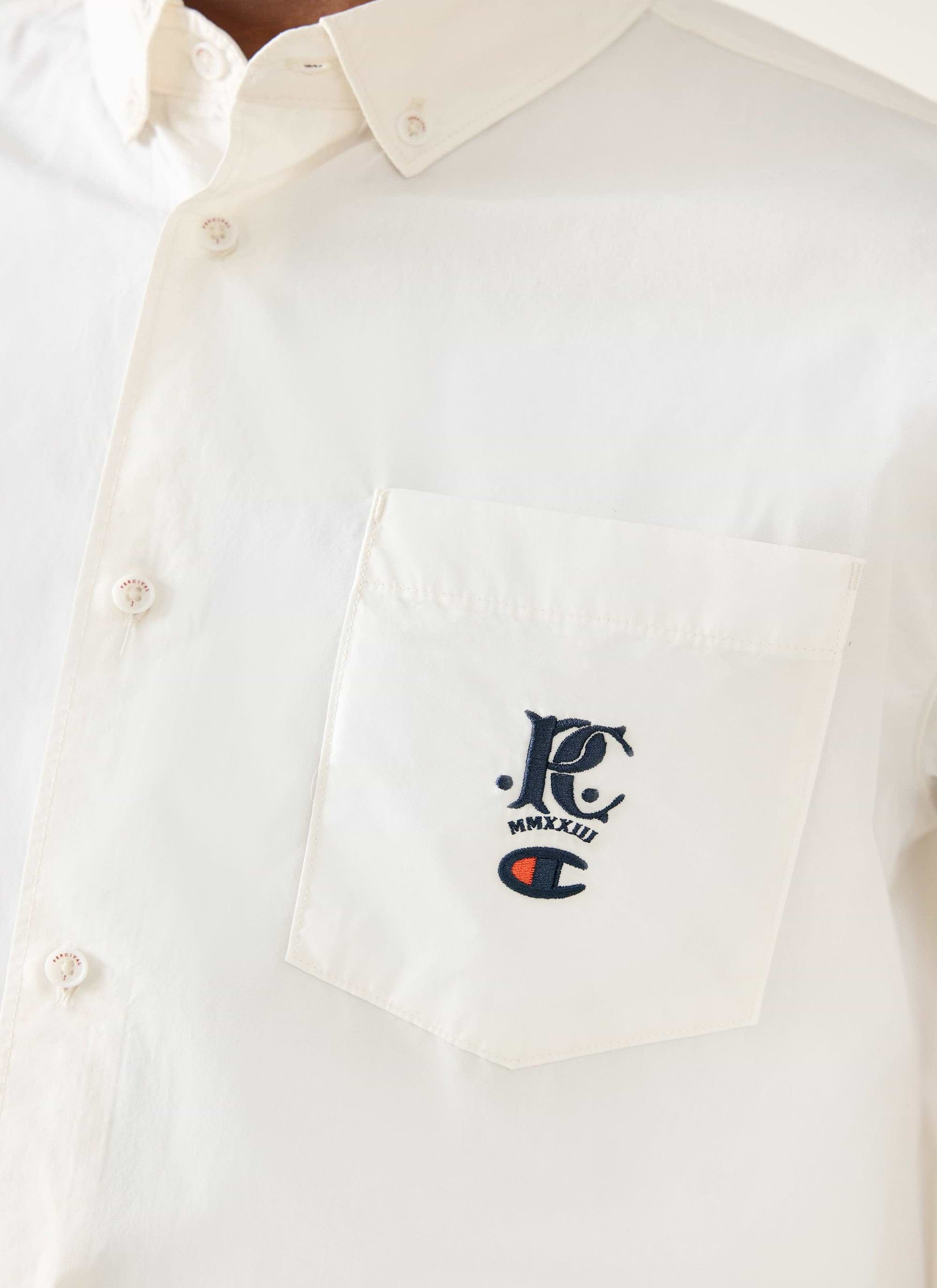 A close-up of the Champion x Percival embroidery on the chest pocket of the ecru Oxford shirt from Percival.