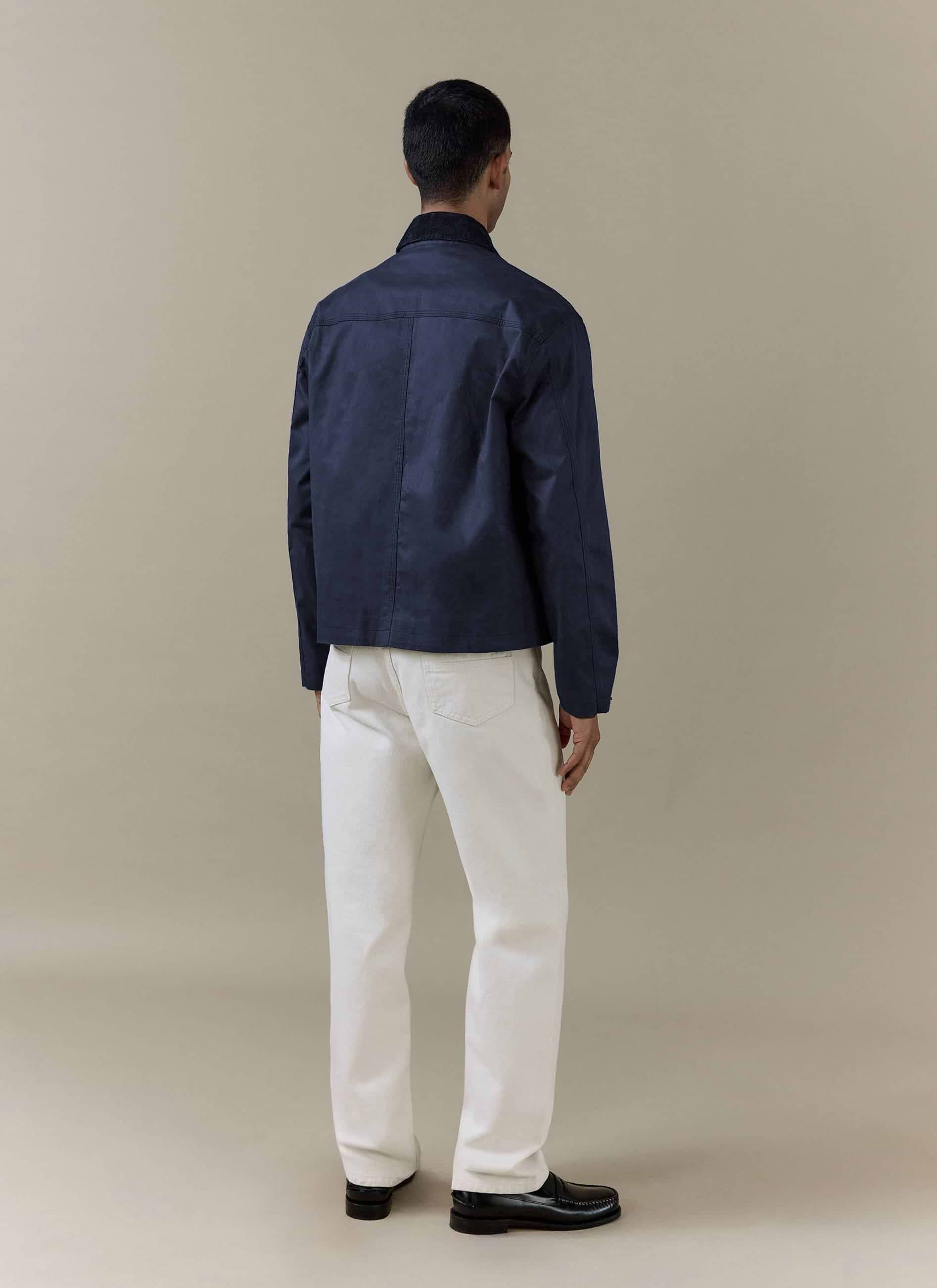 Rear view of the navy blue Percival Wax Zip Jacket in waxed cotton, styled with off-white trousers.