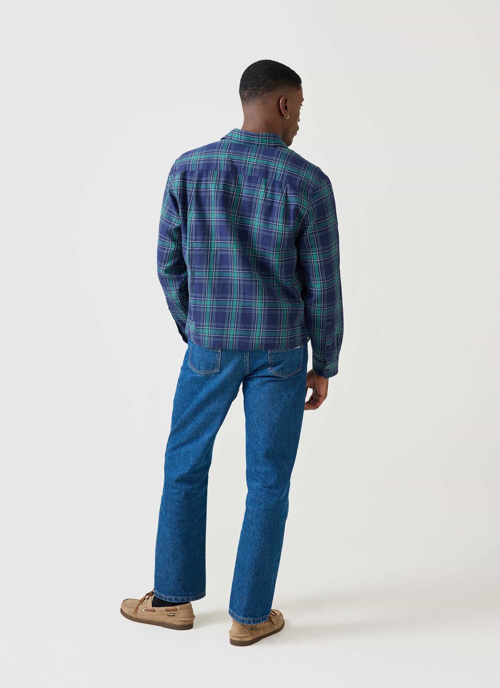 Rear view of a model wearing the Percival x Champion check boxy shirt in blue and green, styled with denim jeans.