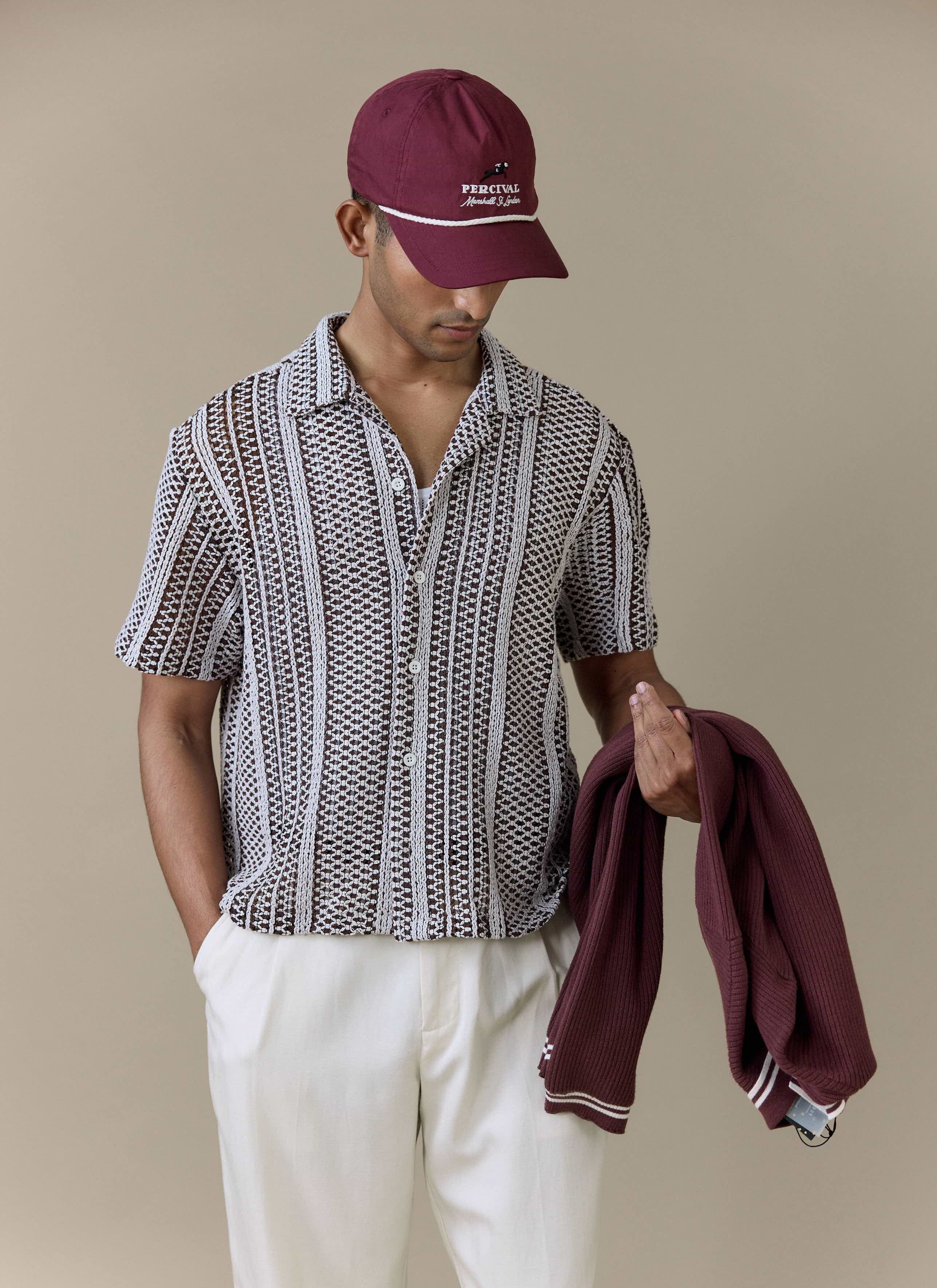 Model wearing the brown Hugh Crochet Boxy Shirt by Percival, styled with a maroon Percival cap and white trousers.