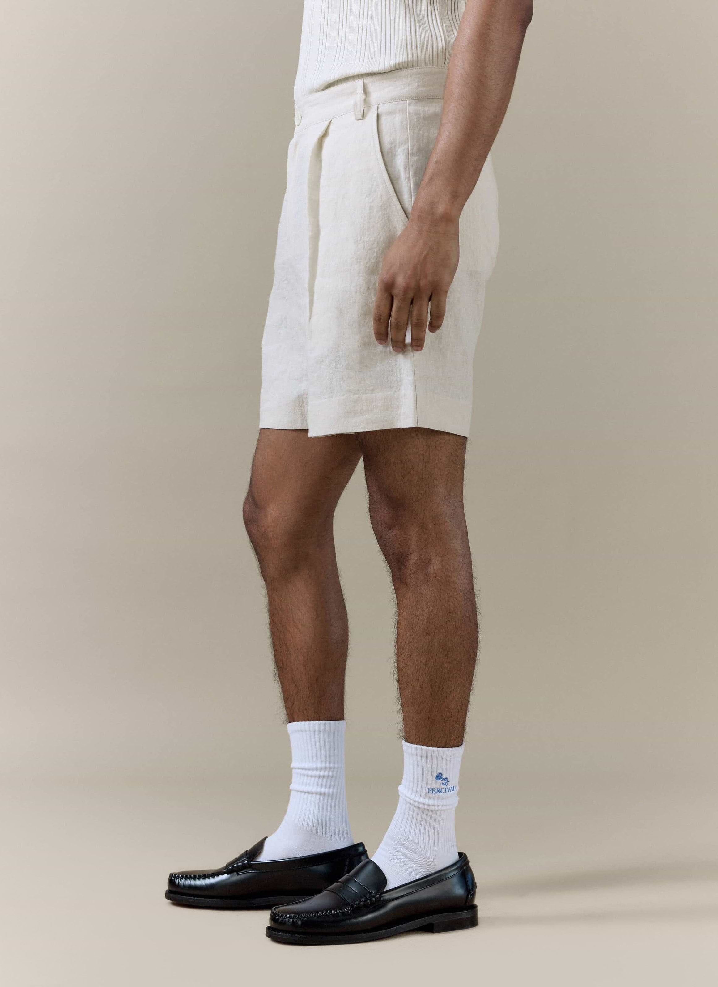 Percival Pleated Linen Shorts in cream, styled with white logo socks and black leather loafers.
