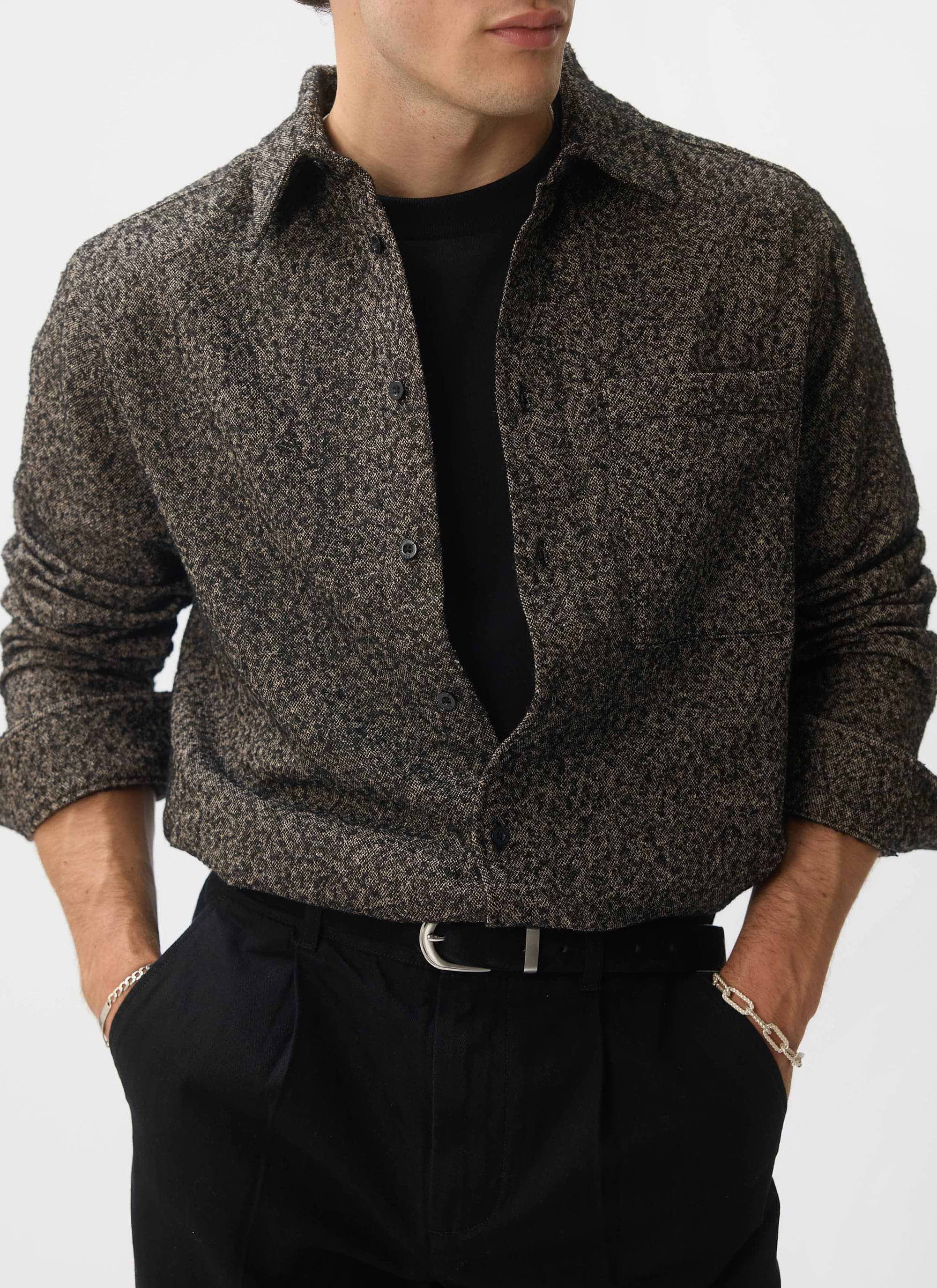 A model wears the Percival Blyton Long Sleeve Shirt in grey, styled open over a black t-shirt and black trousers.