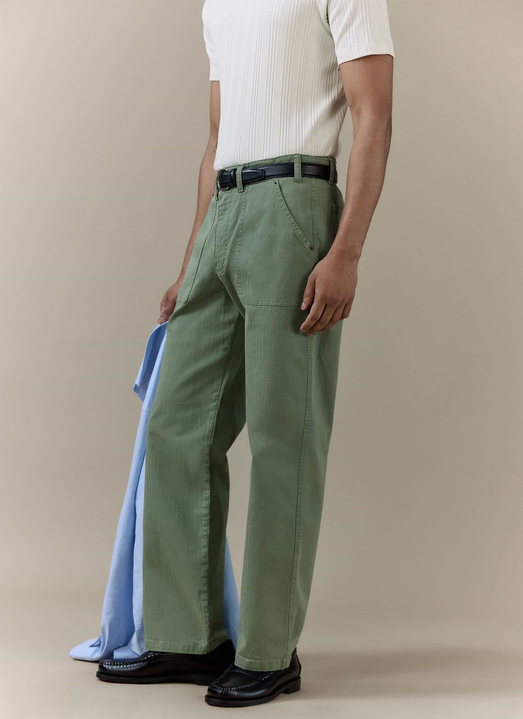 Percival Lungo Herringbone Straight Trousers in sage cotton, styled with a white ribbed shirt and black loafers.